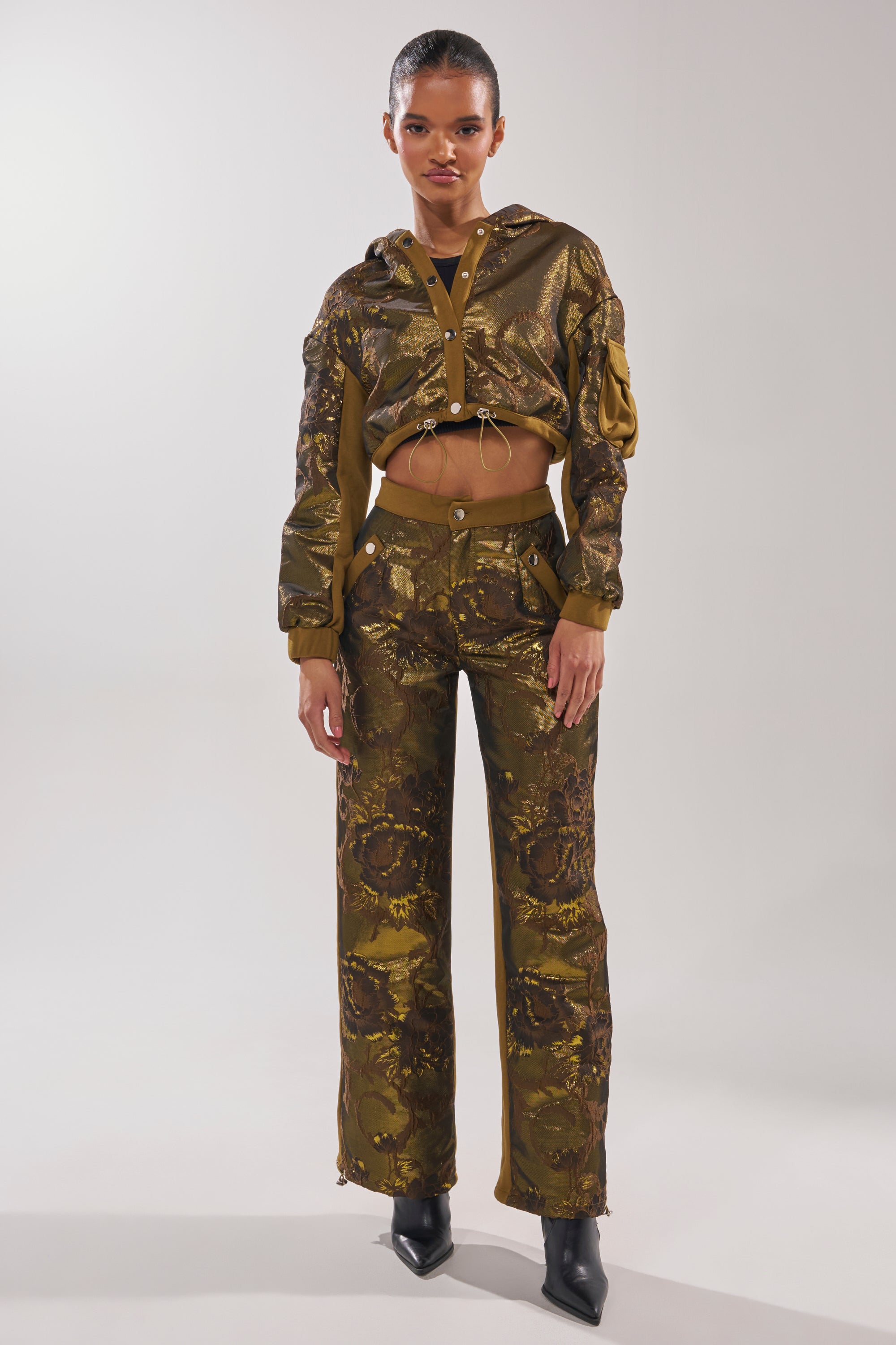 A woman models the YOU KNOW IT BABY CROP BUTTON DOWN—an olive green and brown floral brocade jacket with matching high-waisted pants and black pointed-toe boots—against a white background, highlighting chic streetwear style. 6