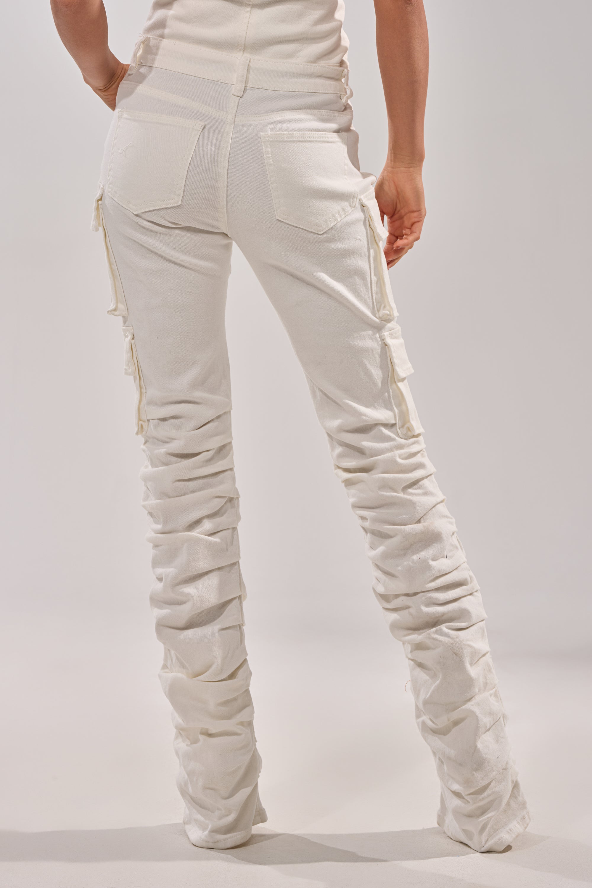 A person stands facing away, wearing the IT GETS EASIER STACKED CARGO PANT IN WHITE with pockets and a matching fitted top, set against a plain light background. 5