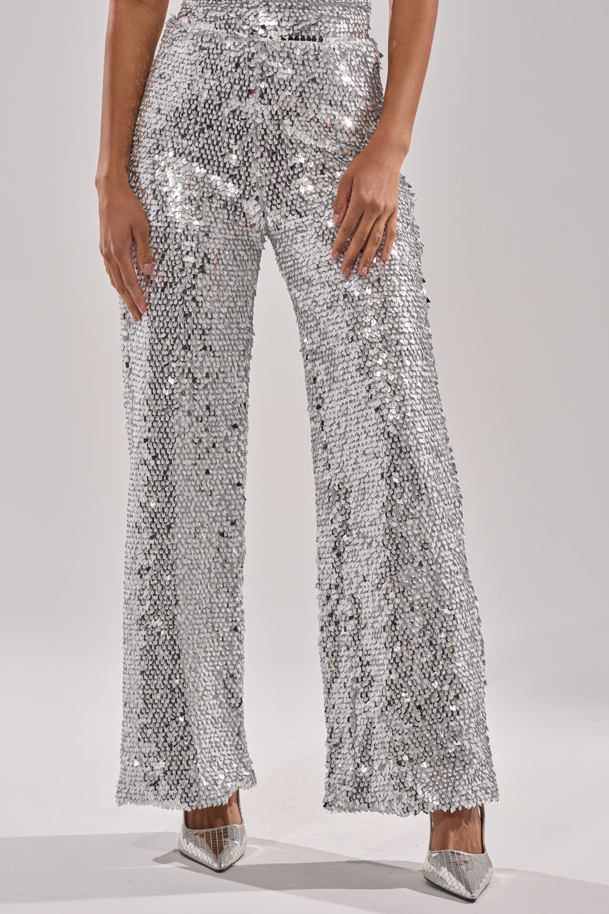 A person wearing NYE GIRLY TROUSER sequin embellished wide-leg pants and silver pointed-toe heels stands against a plain light background, hands resting at their sides. 2