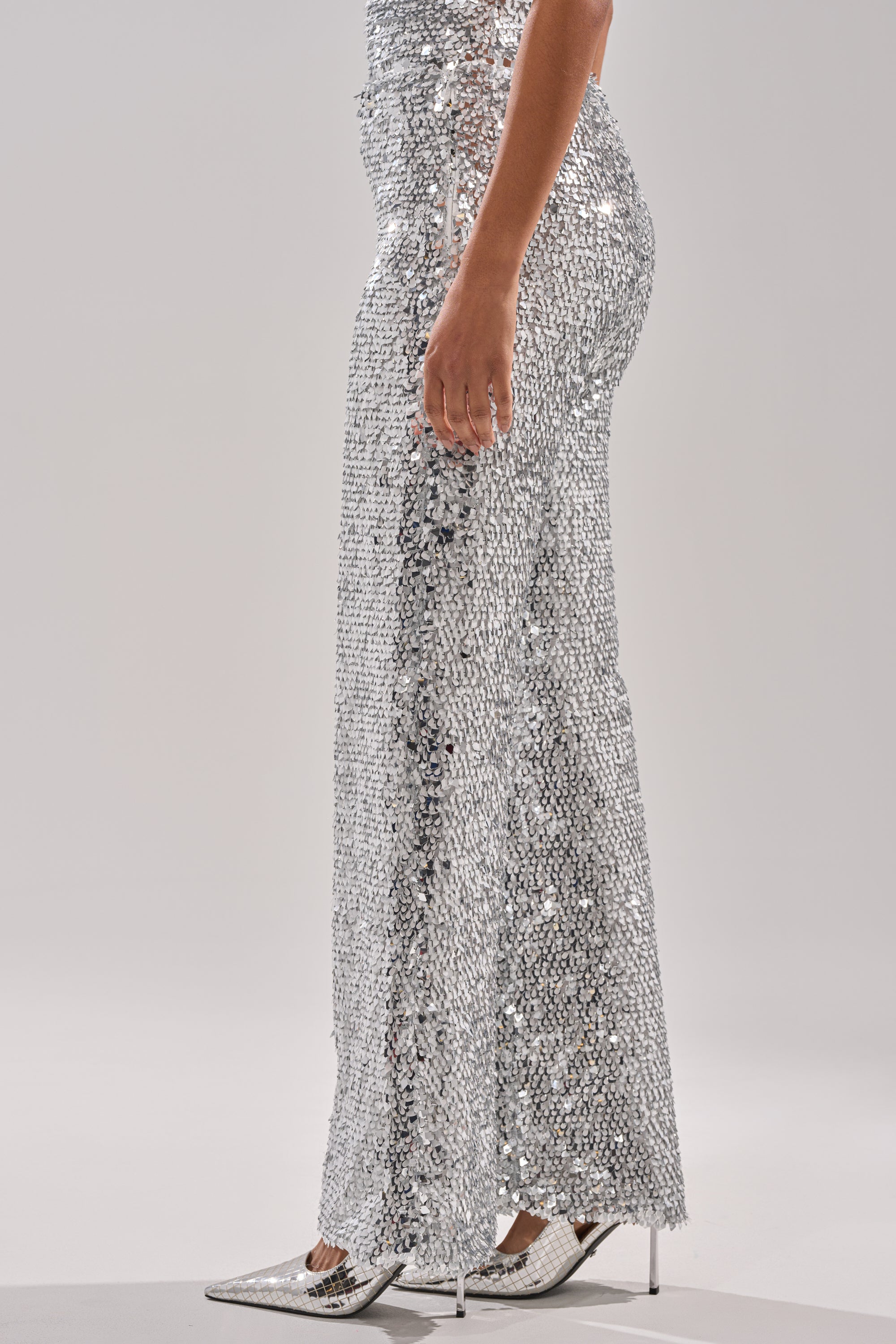 A person models the NYE GIRLY TROUSER with metallic sequins and matching pointed heels, standing against a plain light background; only the lower body is visible. 3