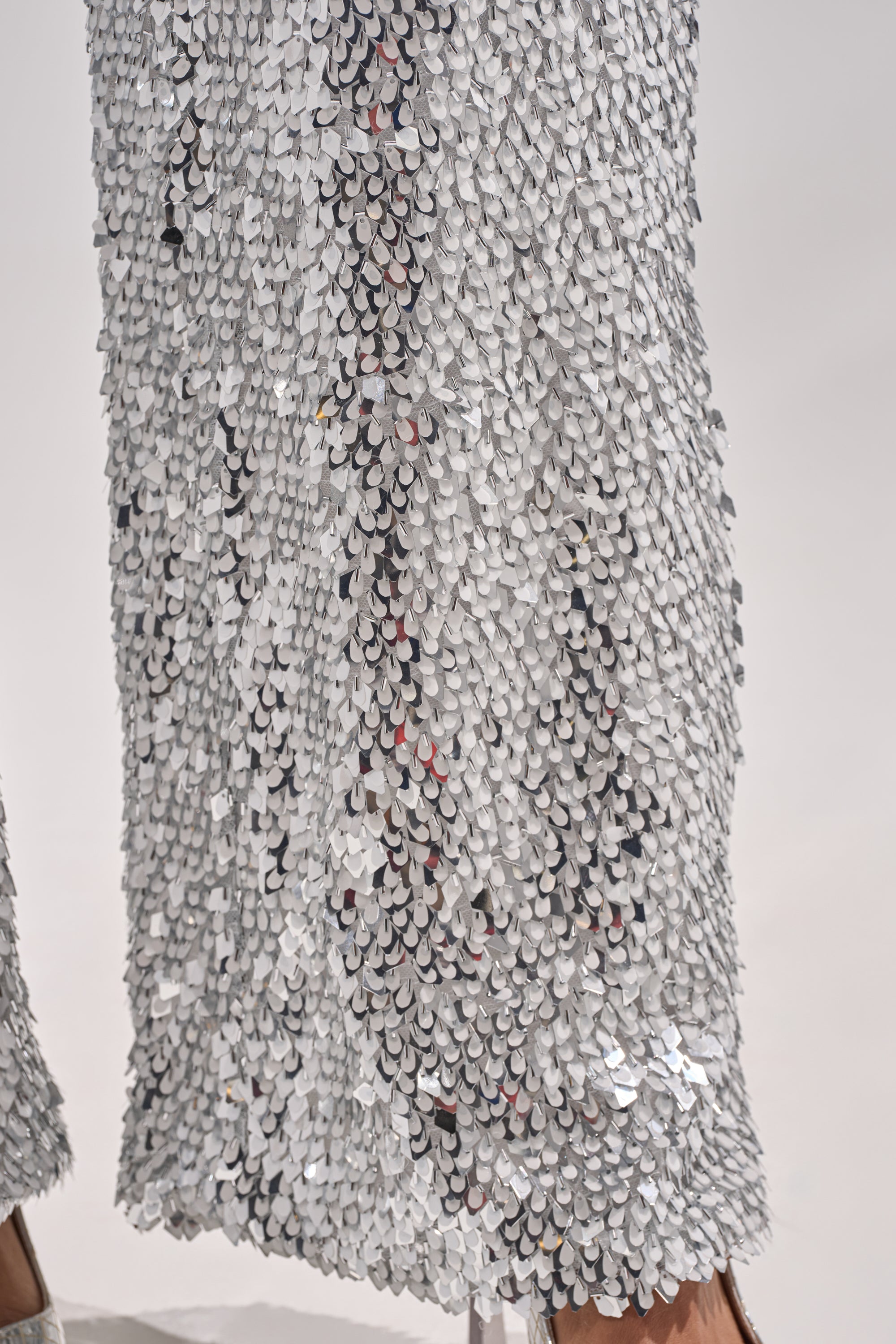 Close-up of NYE GIRLY TROUSER: wide-leg pants covered in densely packed, shiny silver sequins that reflect light for a textured, shimmering effect—perfect statement metallic sequin pants for standout New Year's style. Hem and shoe partly visible. 7