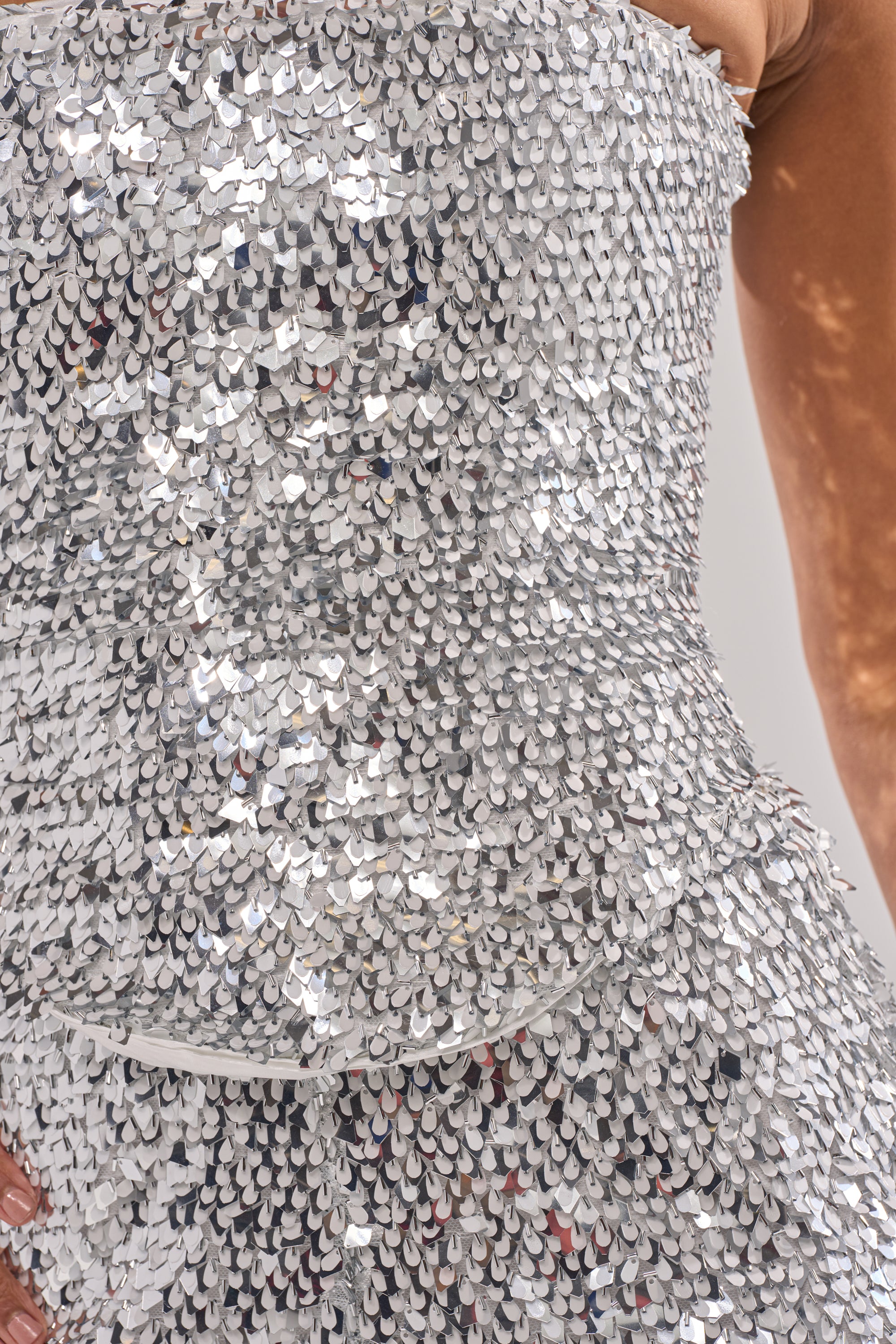 Close-up of a person wearing the NYE GIRLY CORSET, a strapless, form-fitting top covered in shiny silver sequins for a shimmering look. The person's hand rests on their hip.