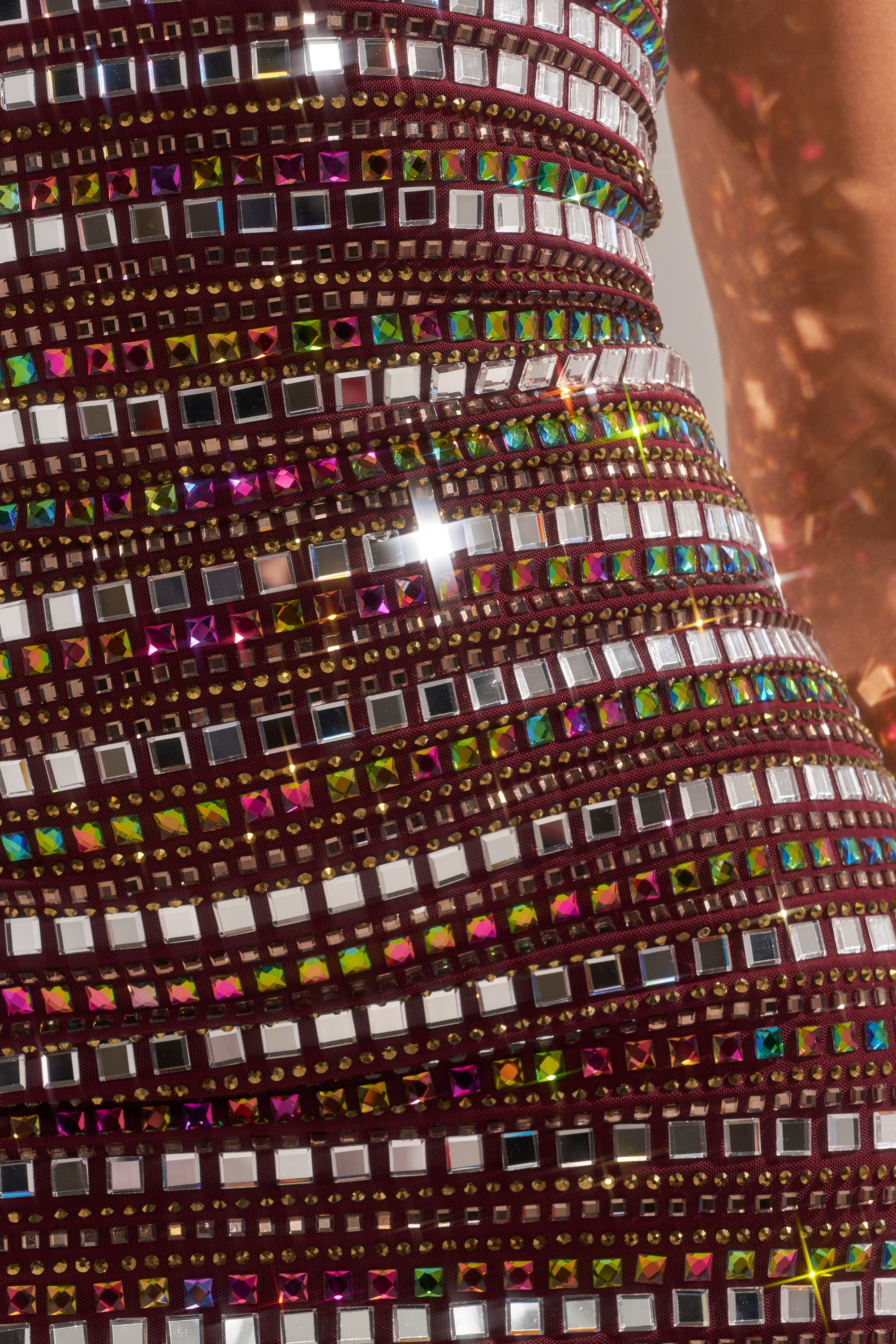 Close-up of the LOOK AT HER GLOW RHINESTONE MINI DRESS, featuring rows of square, multi-colored reflective gems and sequins on maroon fabric, sparkling brilliantly in the light. 12