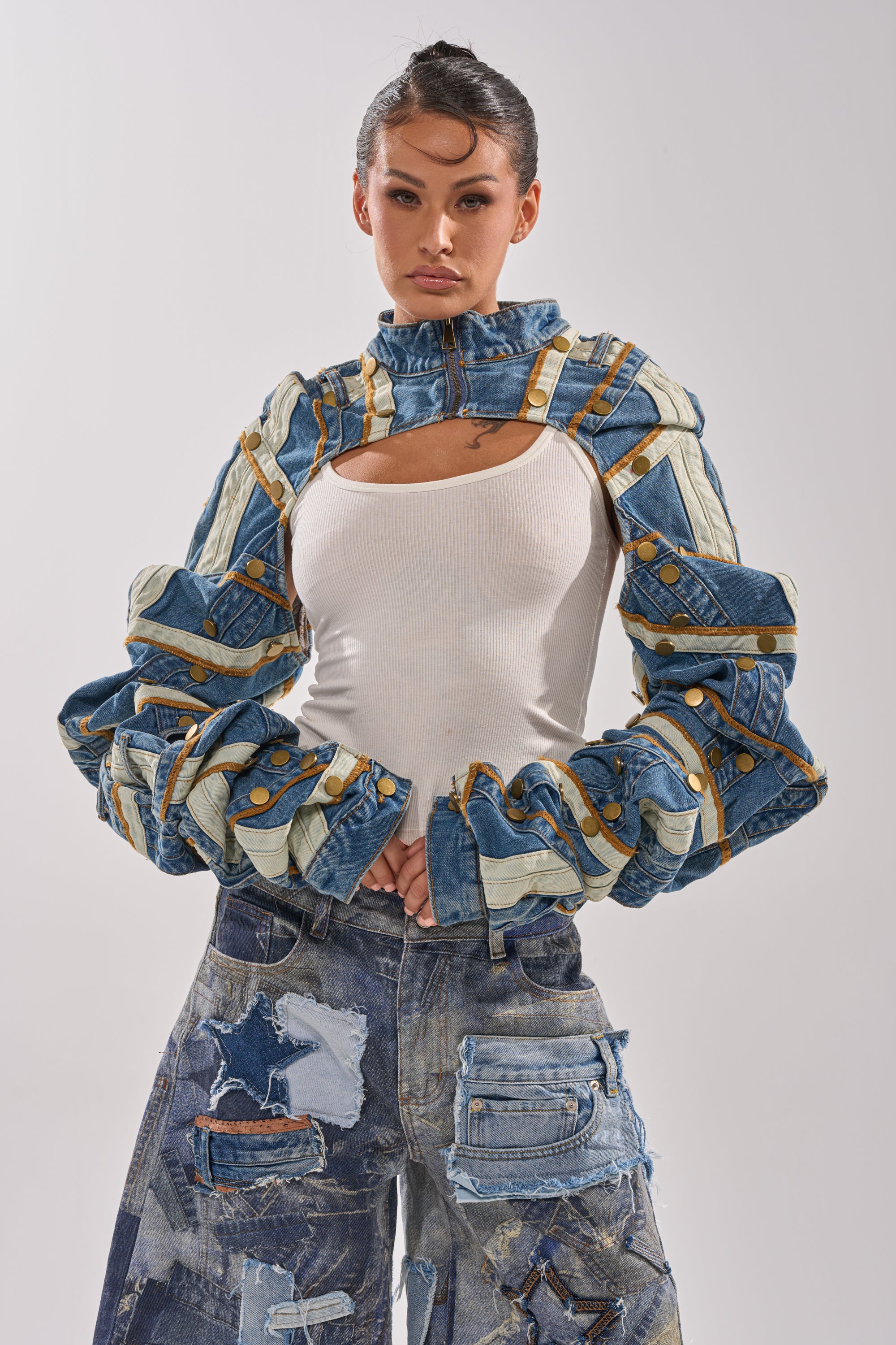 A woman poses in a white tank top, STACKED UP DENIM BOLERO with layered strips and gold buttons, and high-waisted patchwork denim jeans with large pockets in various shades. 3