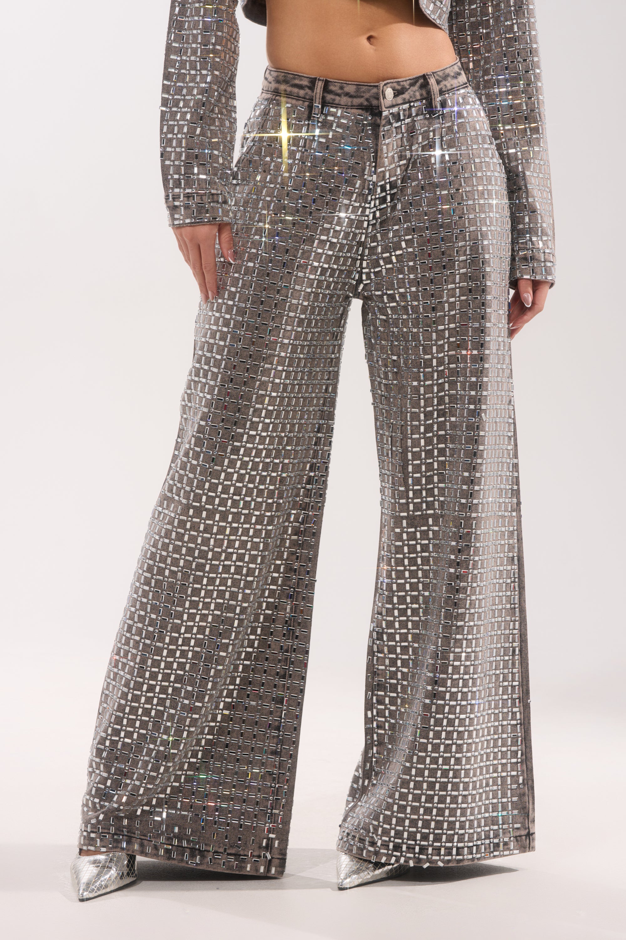 A person wears the PICK N CHOOSE RHINESTONE WIDE LEG DENIM IN GREY, styled with a matching top and pointed silver shoes for a shiny evening look. The photo is cropped from shoulders to feet. 1