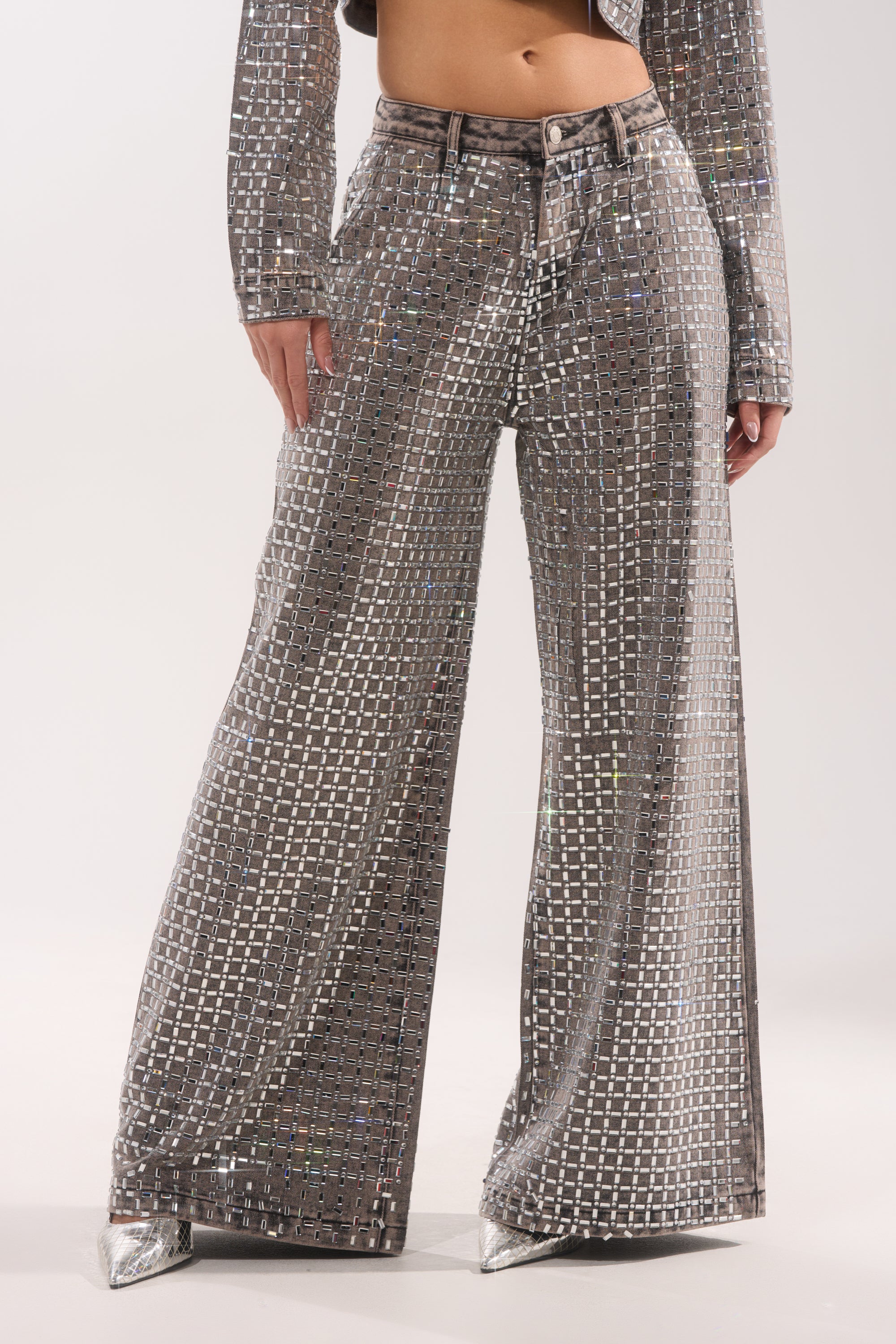 Wearing the PICK N CHOOSE RHINESTONE WIDE LEG DENIM IN GREY, styled with a matching jacket and silver pointed-toe shoes, a person stands against a plain background. 2