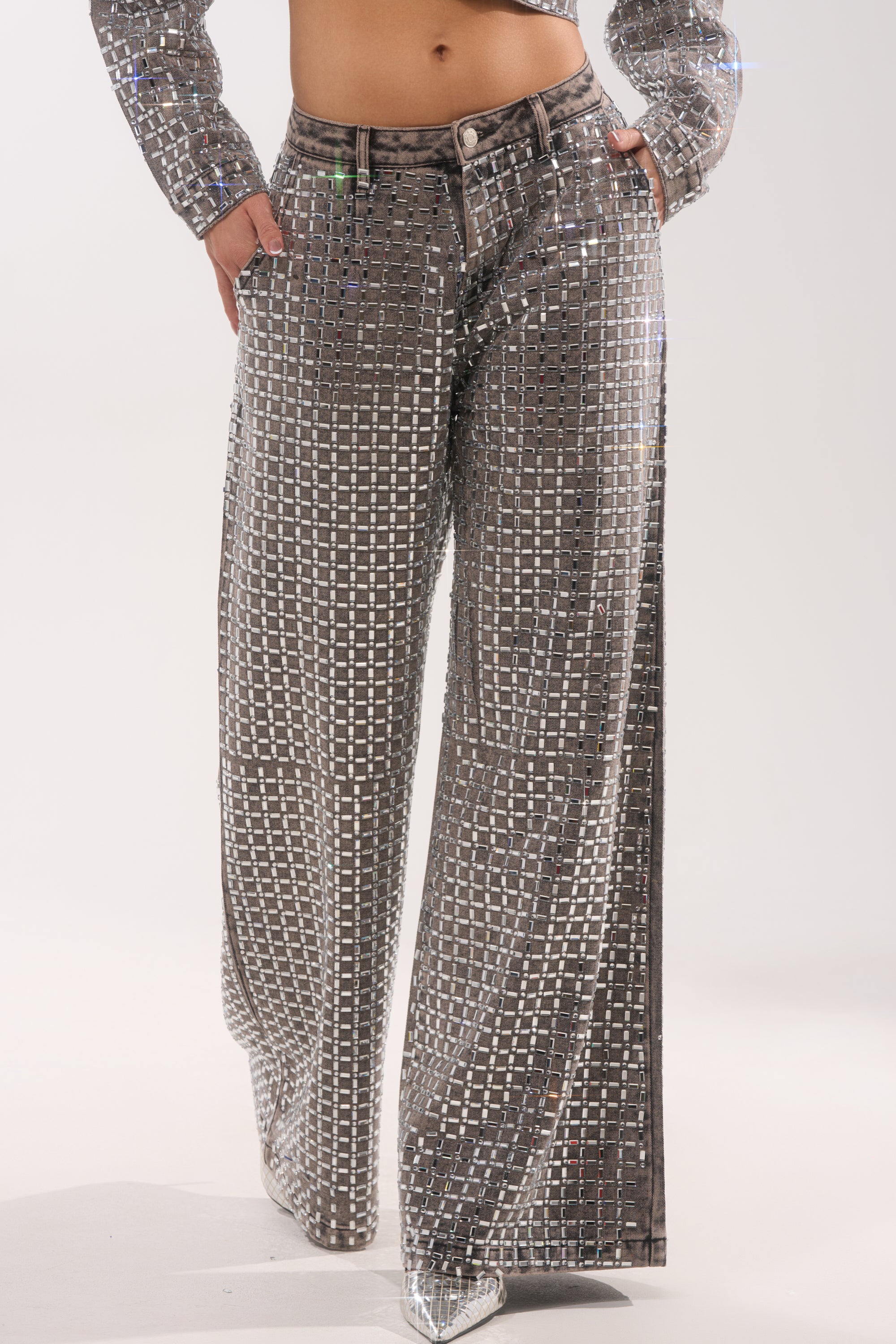 Someone wearing the PICK N CHOOSE RHINESTONE WIDE LEG DENIM IN GREY, covered in reflective rhinestones and paired with a matching cropped jacket, shines with a shimmering, disco-inspired look perfect for evening wear. 3