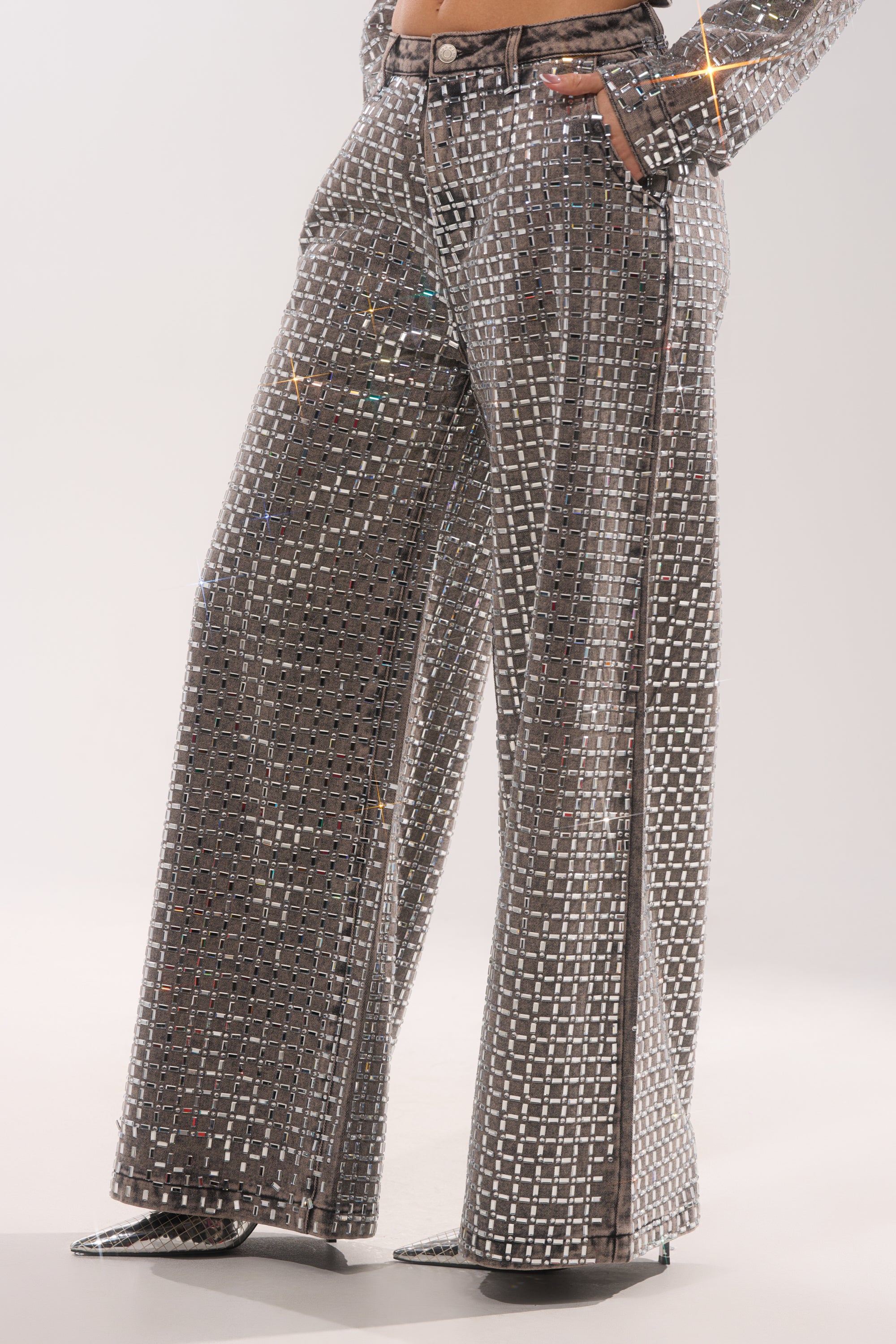 A person wears PICK N CHOOSE RHINESTONE WIDE LEG DENIM IN GREY—shiny, high-waisted wide-leg jeans with a reflective pattern—paired with a matching blazer against a light background, ideal for glitzy evening wear. 4