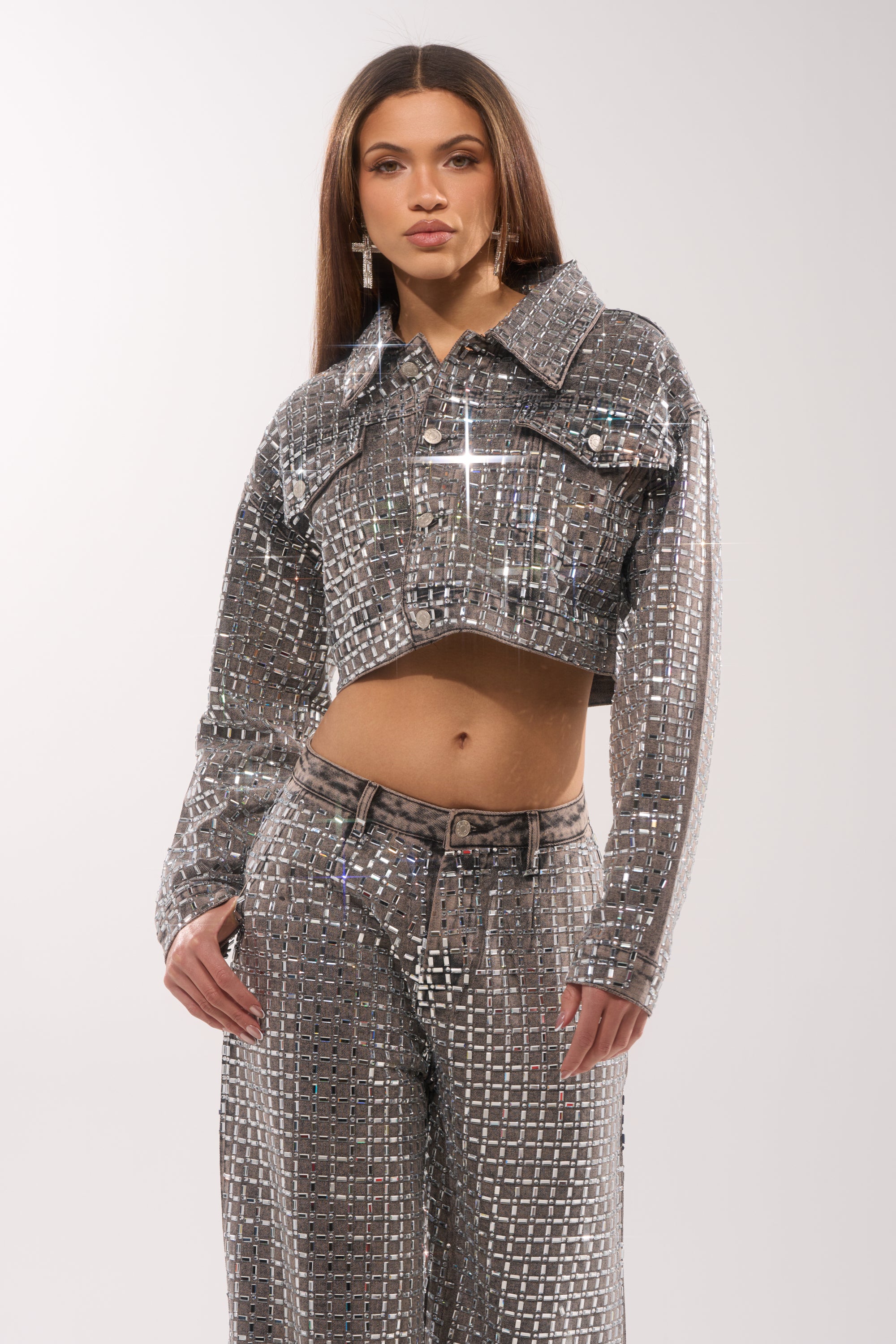 A woman poses in striking street style, wearing the PICK N CHOOSE Rhinestone Denim Jacket in Grey with matching pants. Her long straight hair and a plain light background complete the bold, reflective look. 0