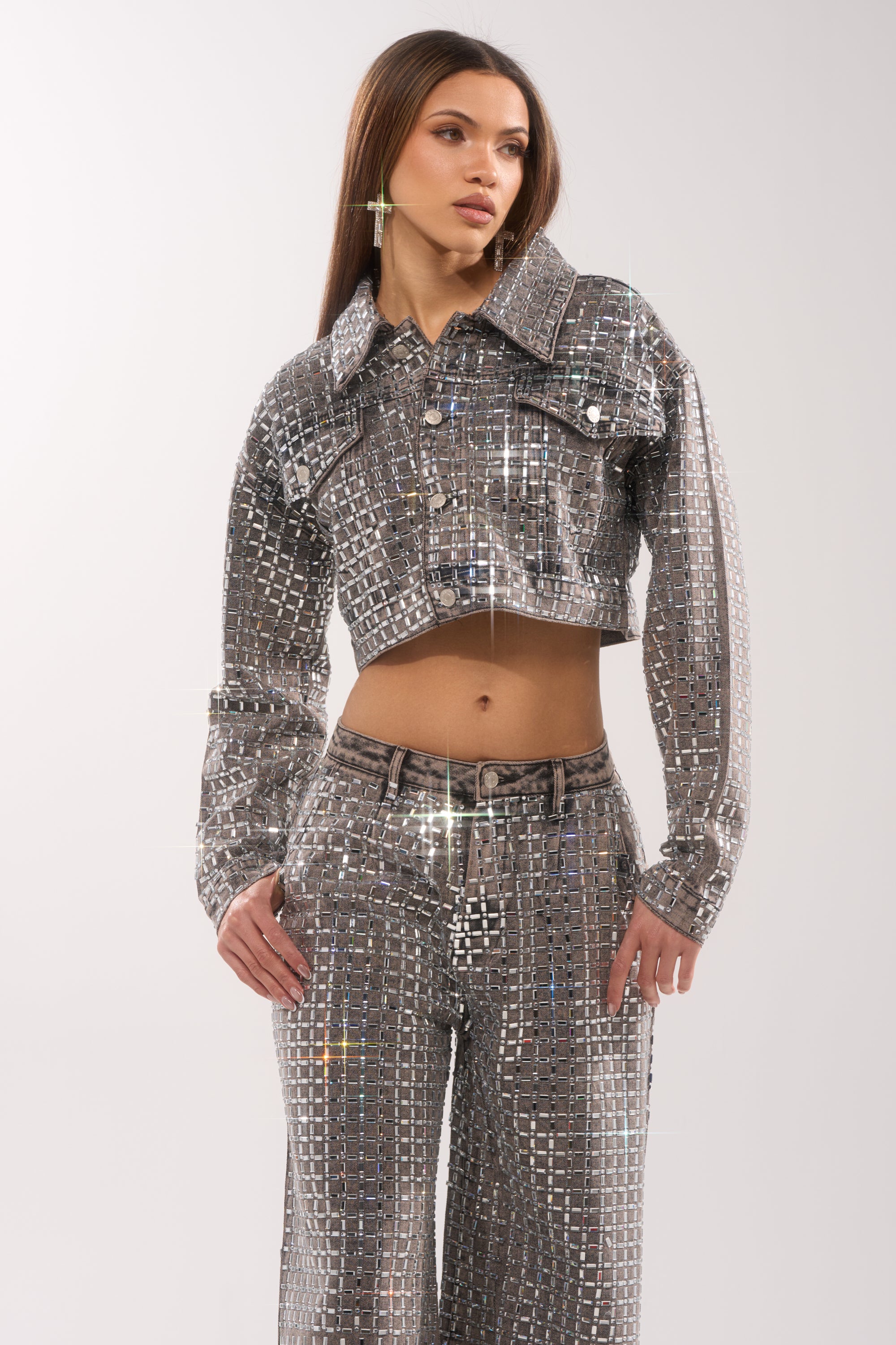 A woman models the PICK N CHOOSE RHINESTONE DENIM JACKET IN GREY over a shiny silver sequin two-piece outfit with high-waisted pants, standing confidently with one hand on her hip against a plain light background. 4