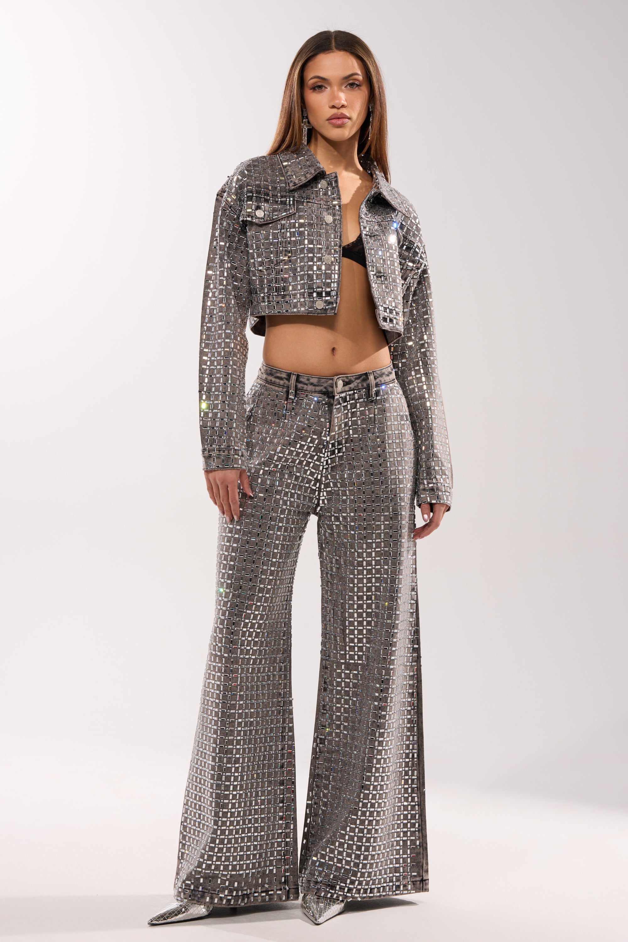 A woman stands confidently against a plain light background in the PICK N CHOOSE RHINESTONE DENIM JACKET IN GREY, styled cropped with matching wide-leg pants and a black bra. 8