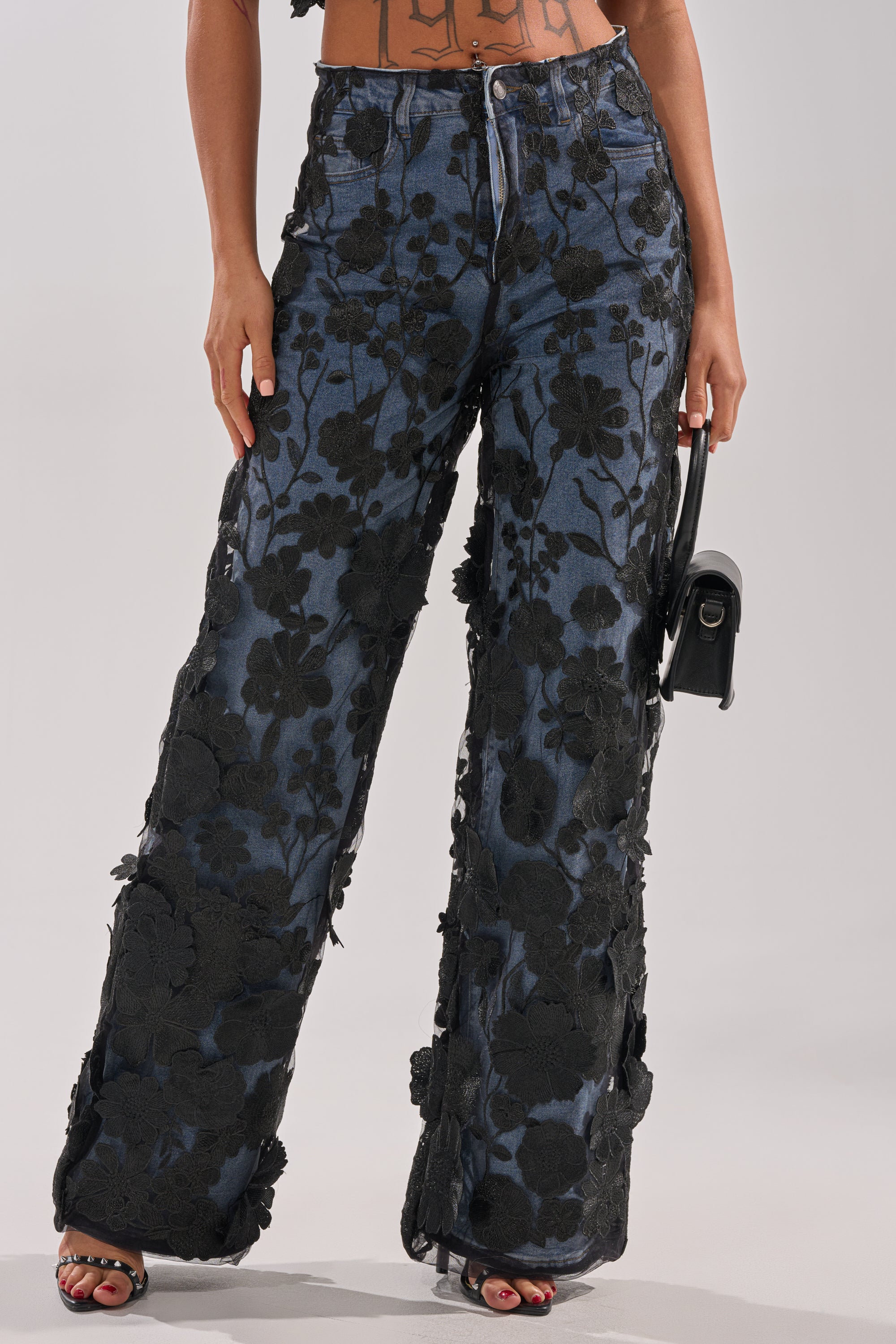 Someone wearing the DONT GIVE UP RELAXED DENIM WITH TULLE OVERLAY, paired with a small black handbag. Only their lower body is visible.