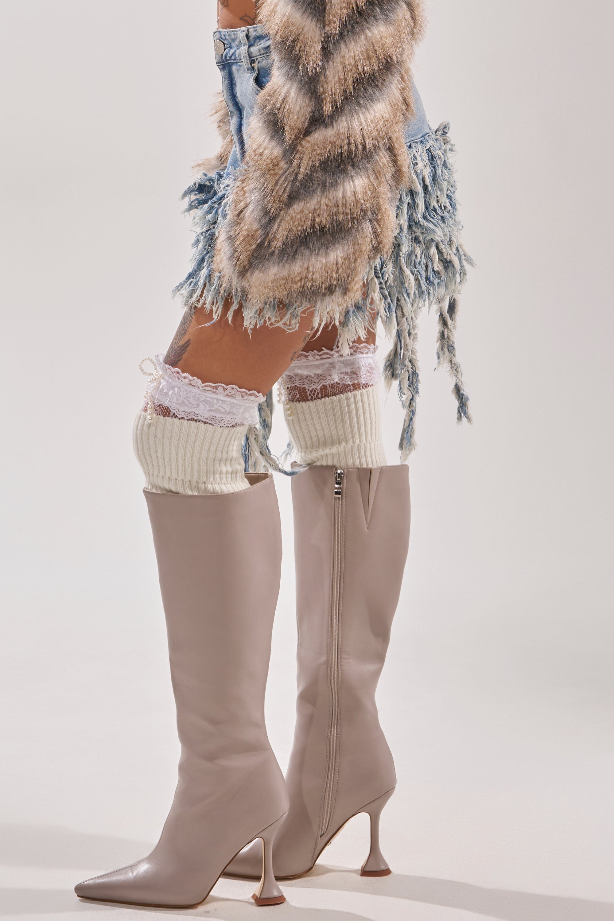 Wearing the OPEN UP YOUR LOVE DENIM SKIRT, light purple knee-high heeled boots, cream lace-trim knit leg warmers, and a faux fur jacket, a person stands against a plain light background. 6