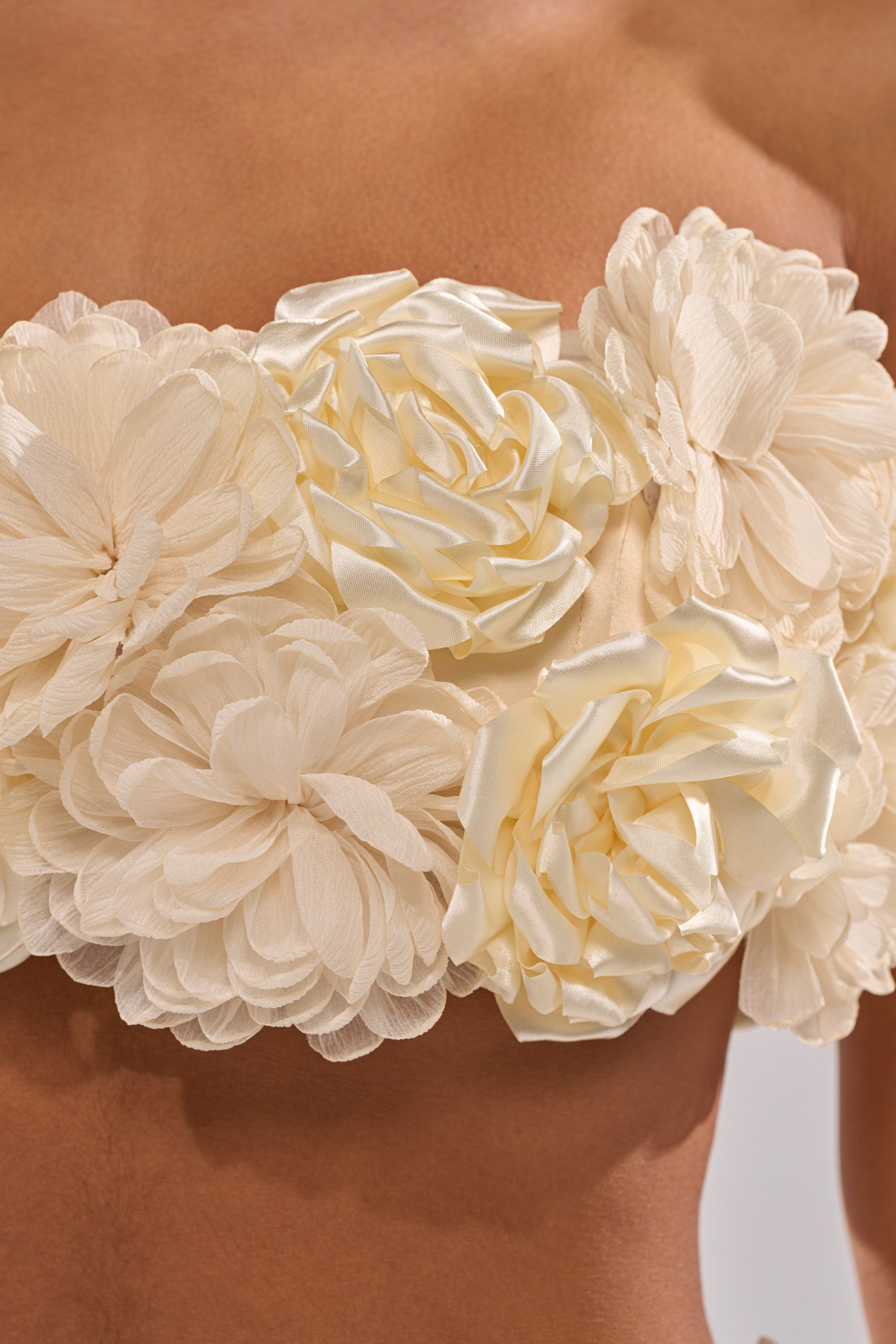 A close-up shows a person wearing the FLOWER POWER BRALETTE, a strapless satin crop top featuring cream 3D floral appliques. The neutral background makes the intricate flowers and textured fabric stand out. 11