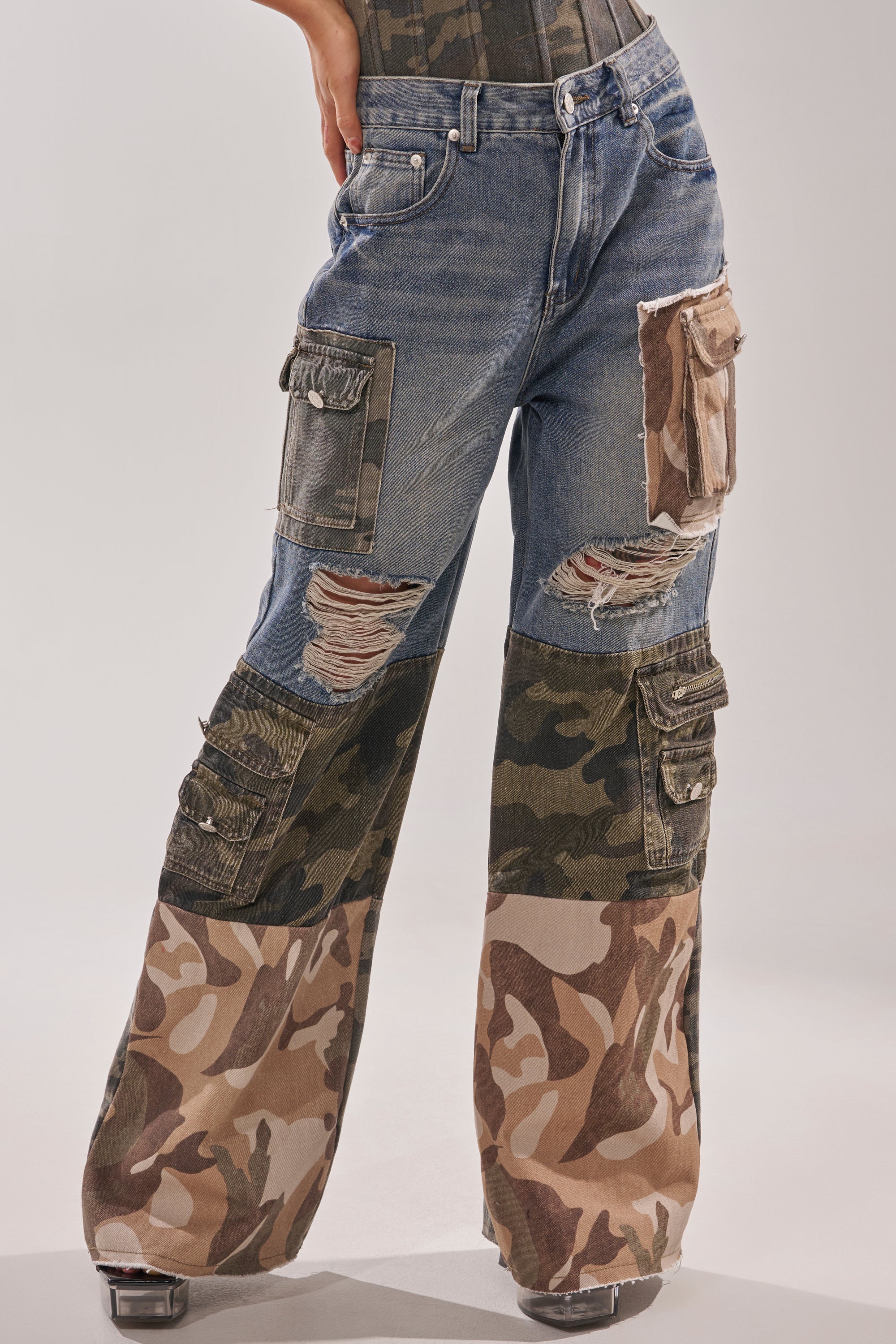 Only the lower body is visible, showing MIXED CAMO DENIM CARGO PANTS with wide-leg fit, cargo pockets, distressed rips, exposed stitching, and multiple camouflage patchwork prints. 2