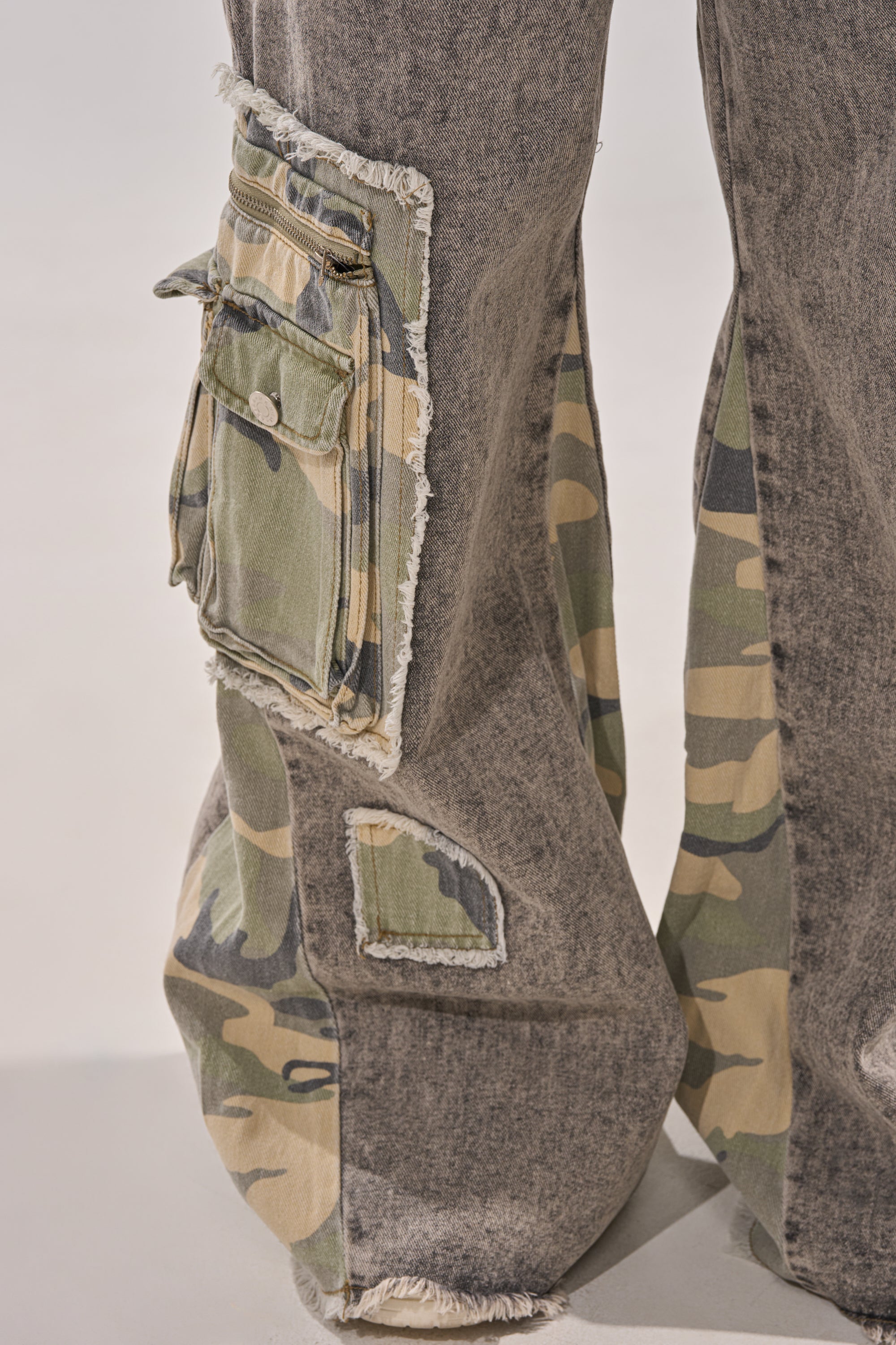 Close-up of DOWN AND DIRTY CAMO CARGO jeans in gray denim, showing frayed edges, camo cargo pockets, and a large upper thigh pocket with zipper and snap closure. 7