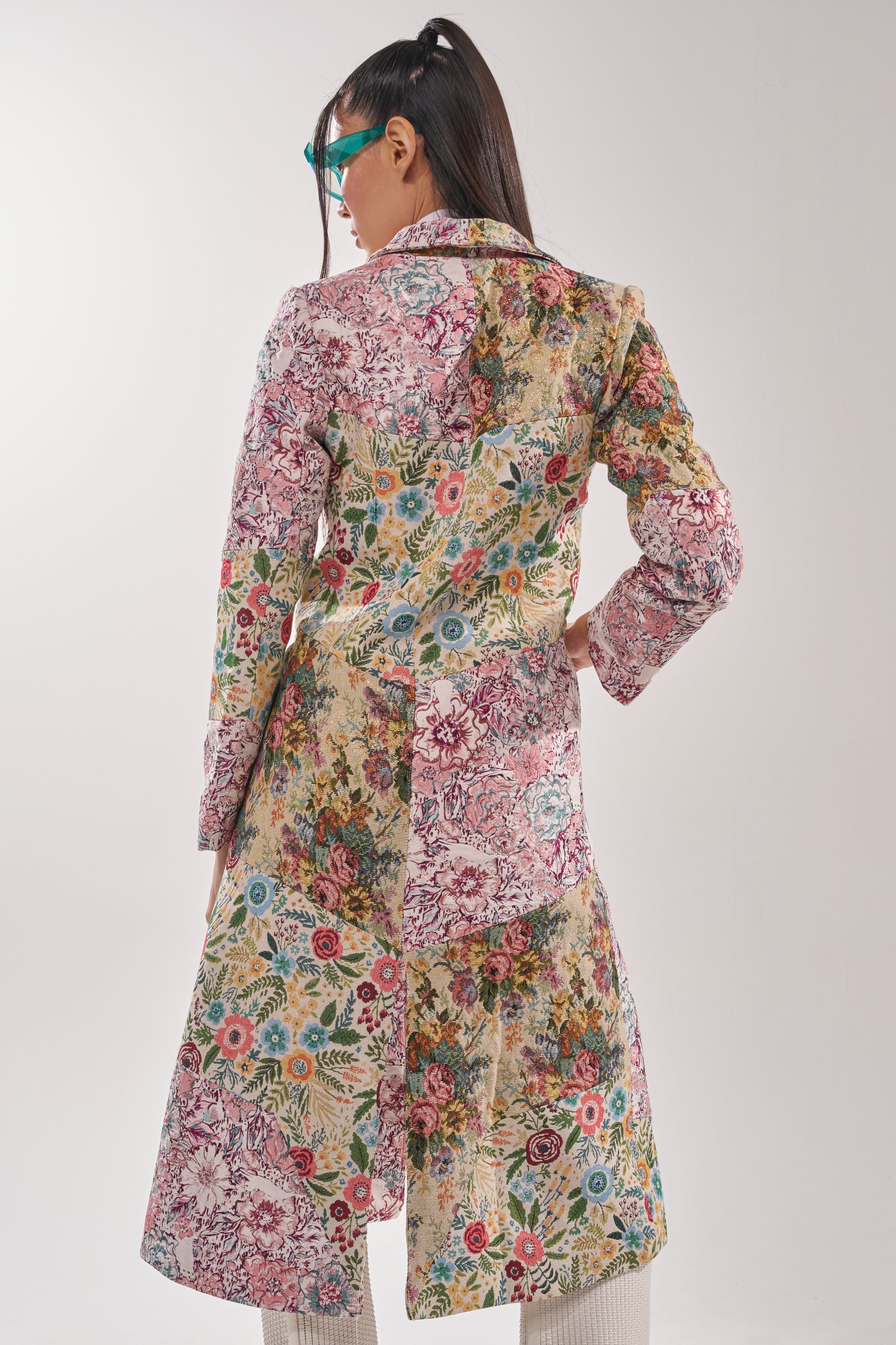 A person in teal sunglasses and the HAD ME AT HELLO PATCHWORK TRENCH stands with their back to the camera against a plain light background. 4