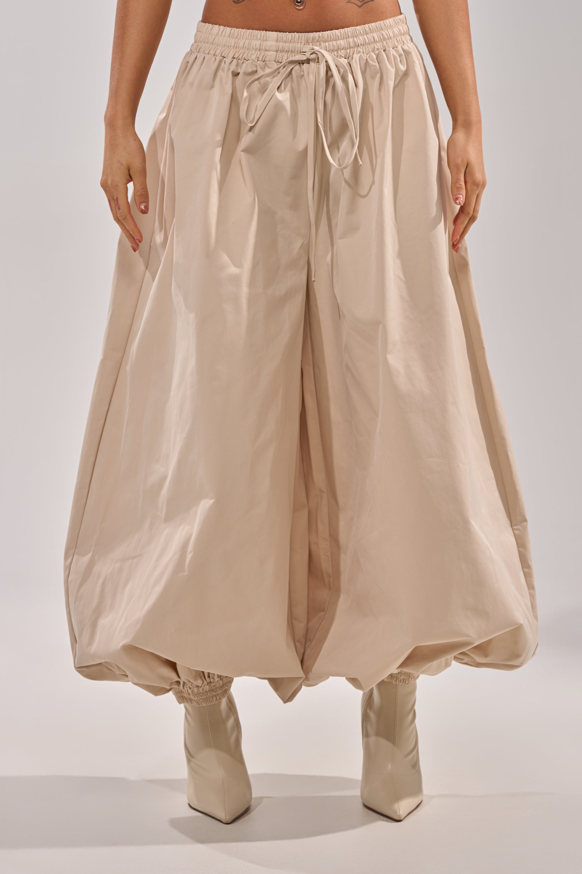 A person wearing the GUESS WHO BALLOON PANT with an elastic waistband and cuffs, paired with pointed-toe beige shoes, stands against a neutral background for a chic street style look. 2