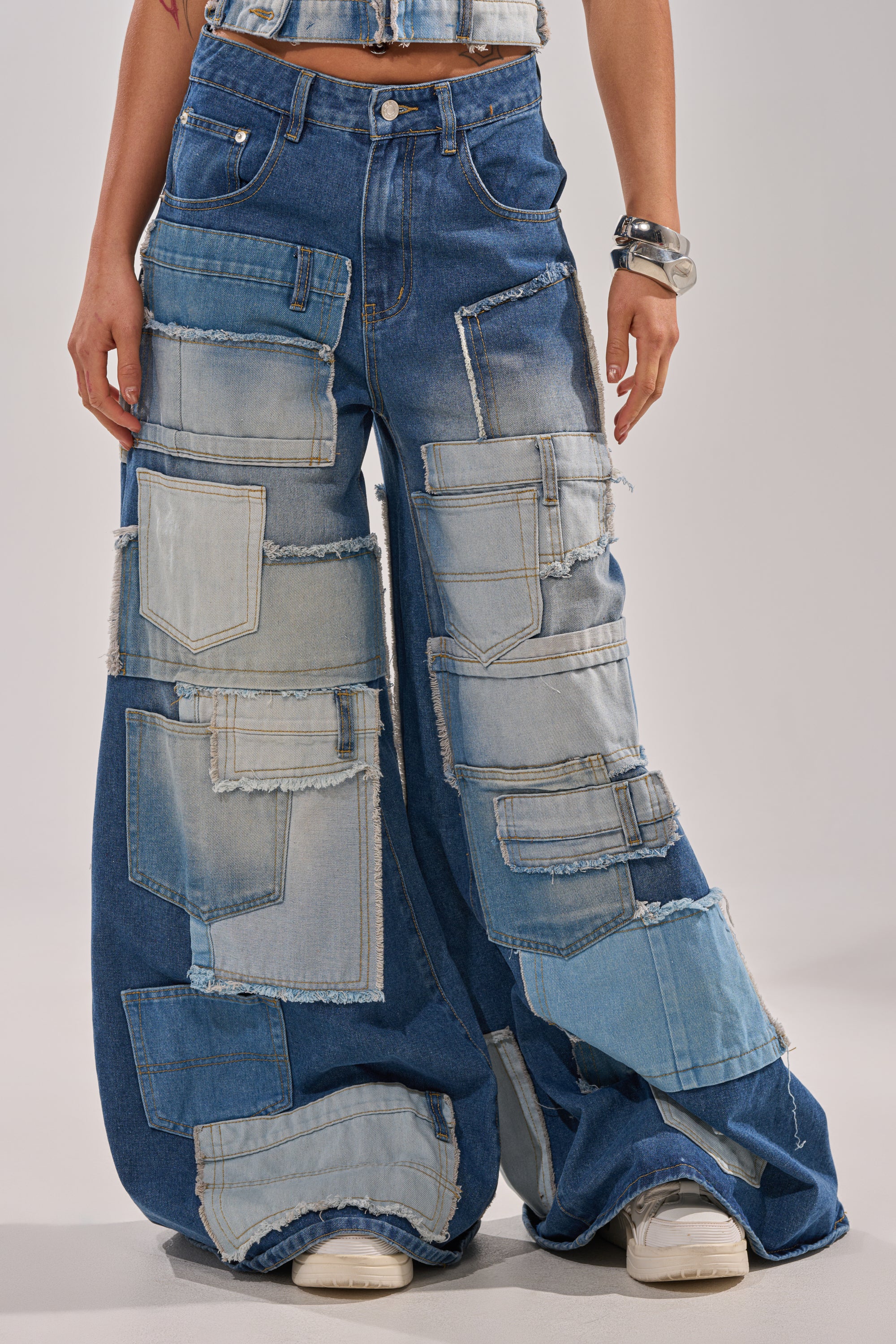 The PATCH ME UP RELAXED DENIM features patchwork wide-leg jeans in various denim shades with frayed edges, styled here with a denim top and white sneakers for a trendy streetwear vibe, shown from the lower torso down. 1