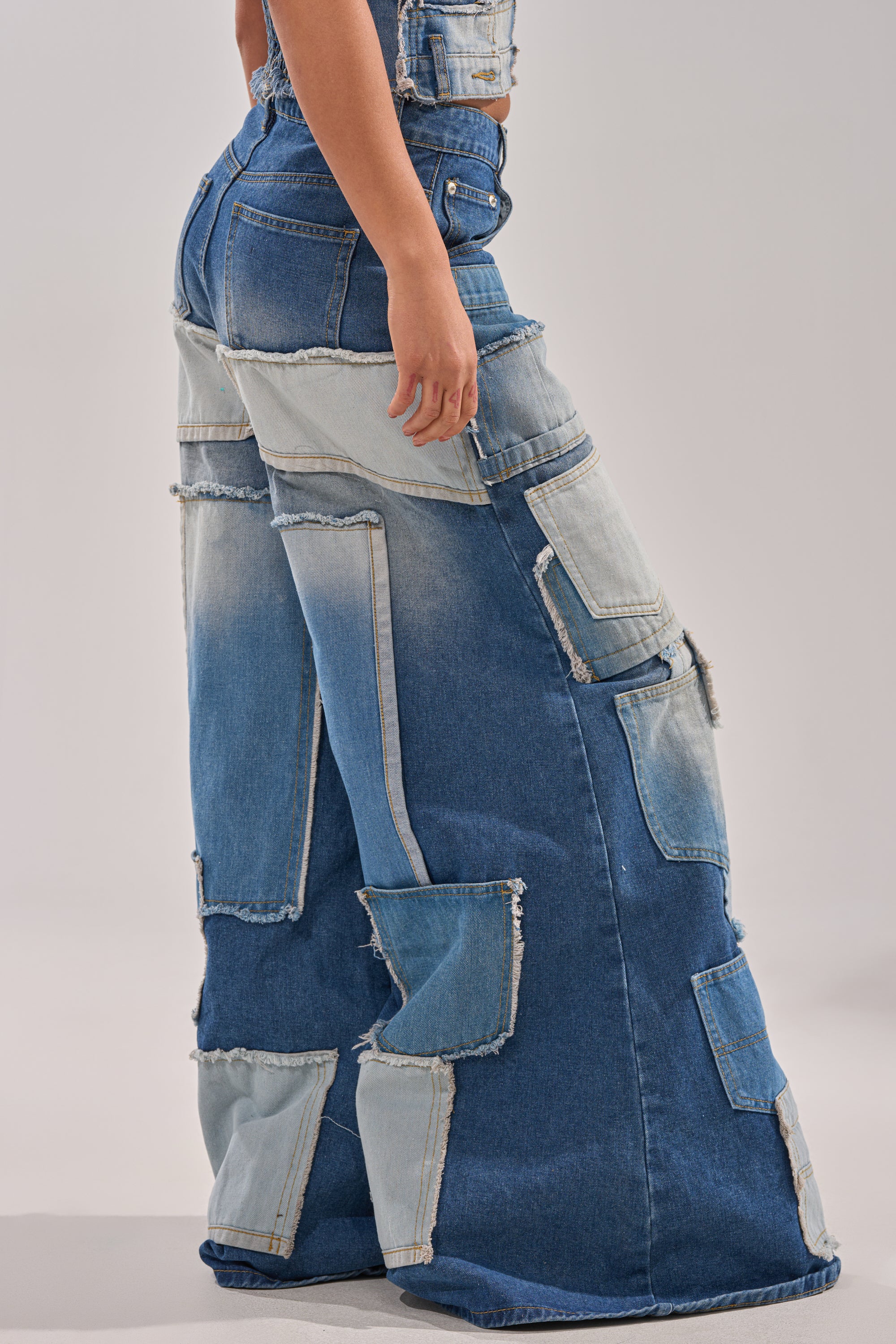 Someone models the PATCH ME UP RELAXED DENIM—patchwork wide-leg jeans in assorted blue shades—against a plain light-gray background. 2