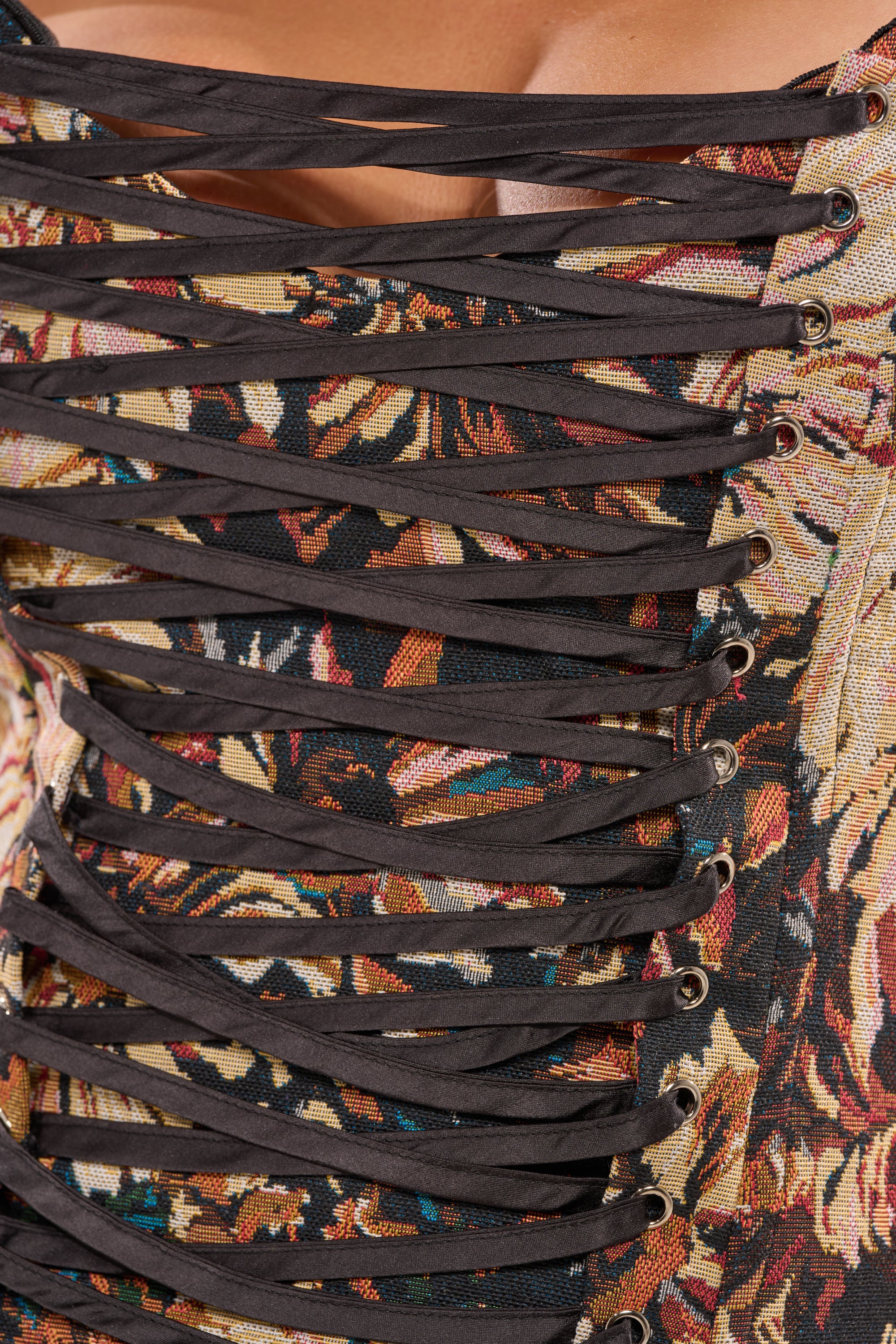 Close-up of the WILD FLORAL TAPESTRY CORSET, featuring colorful floral fabric and structured jacquard design, with black laces threaded through gold eyelets for an elegant finish across the chest. 8