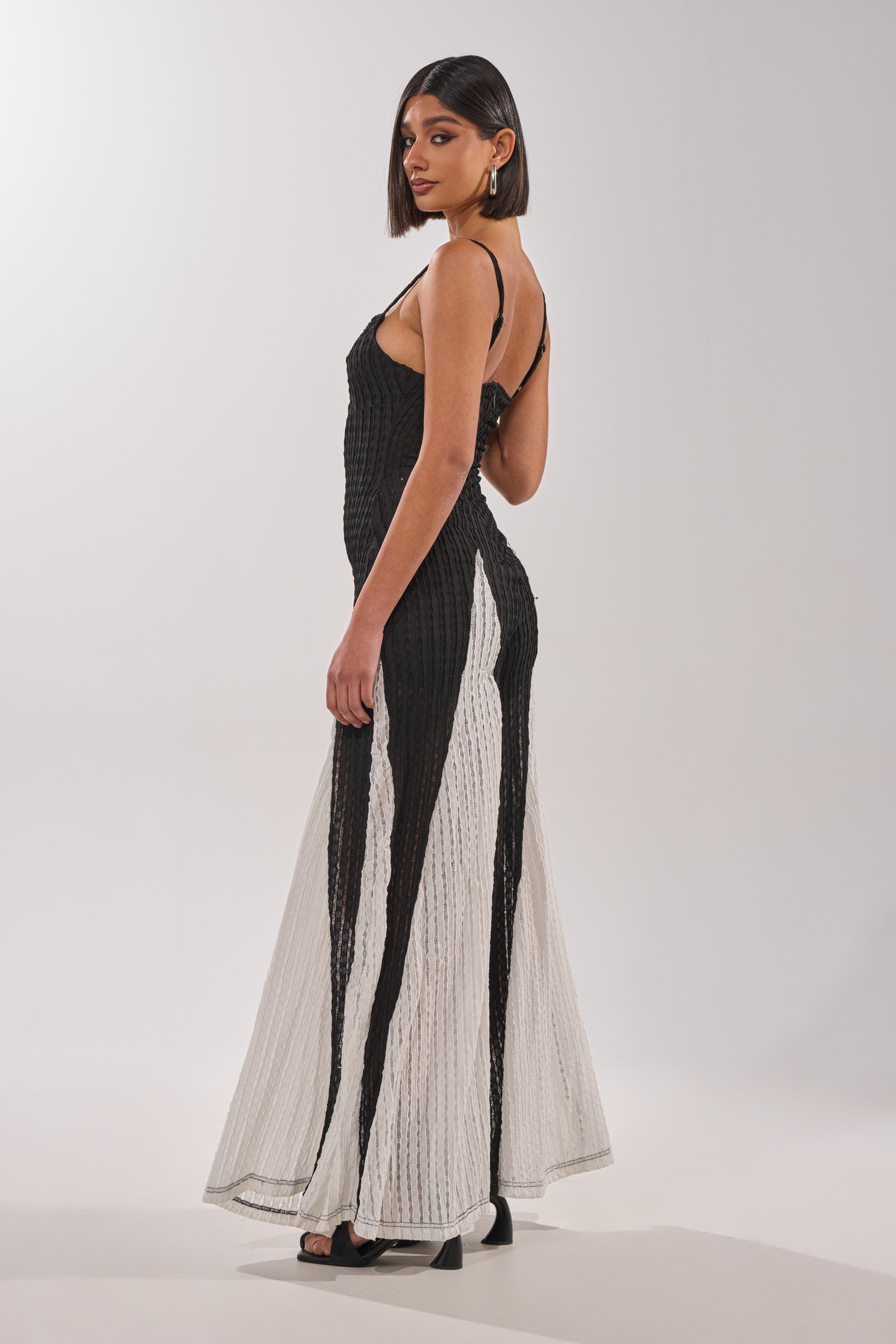 A woman with a sleek bob poses in the ALL DAY EVERYDAY COLOR BLOCK WOVEN JUMPSUIT, a sleeveless, floor-length black and white outfit with flared panels, against a plain light background. 3