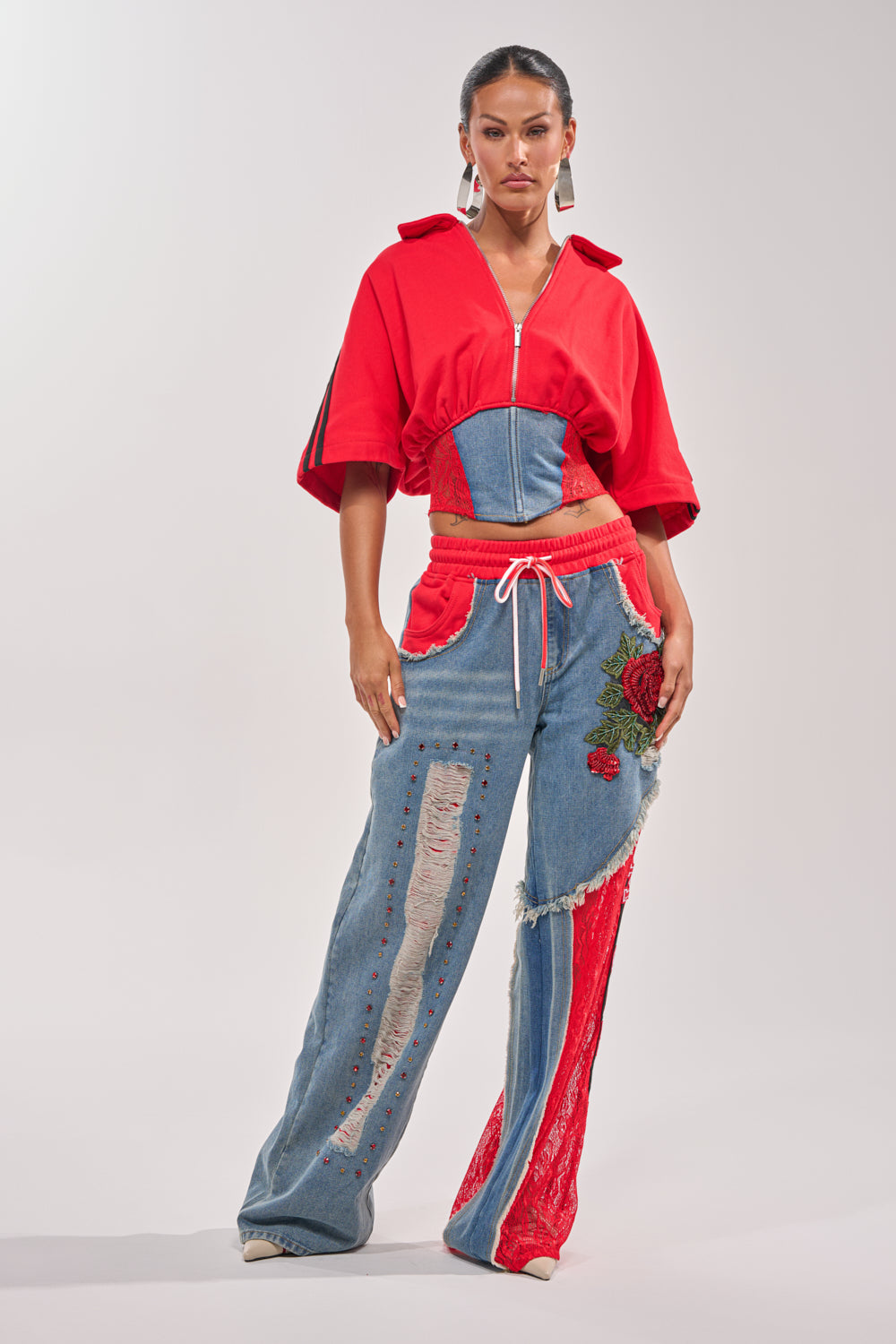 A woman wears the GAME TIME SWEATSHIRT in varsity red with wide sleeves, paired with high-waisted, wide-leg jeans featuring red lace, distressed denim patches, and embroidered rose details. She accessorizes with hoop earrings and a pulled-back hairstyle. 4