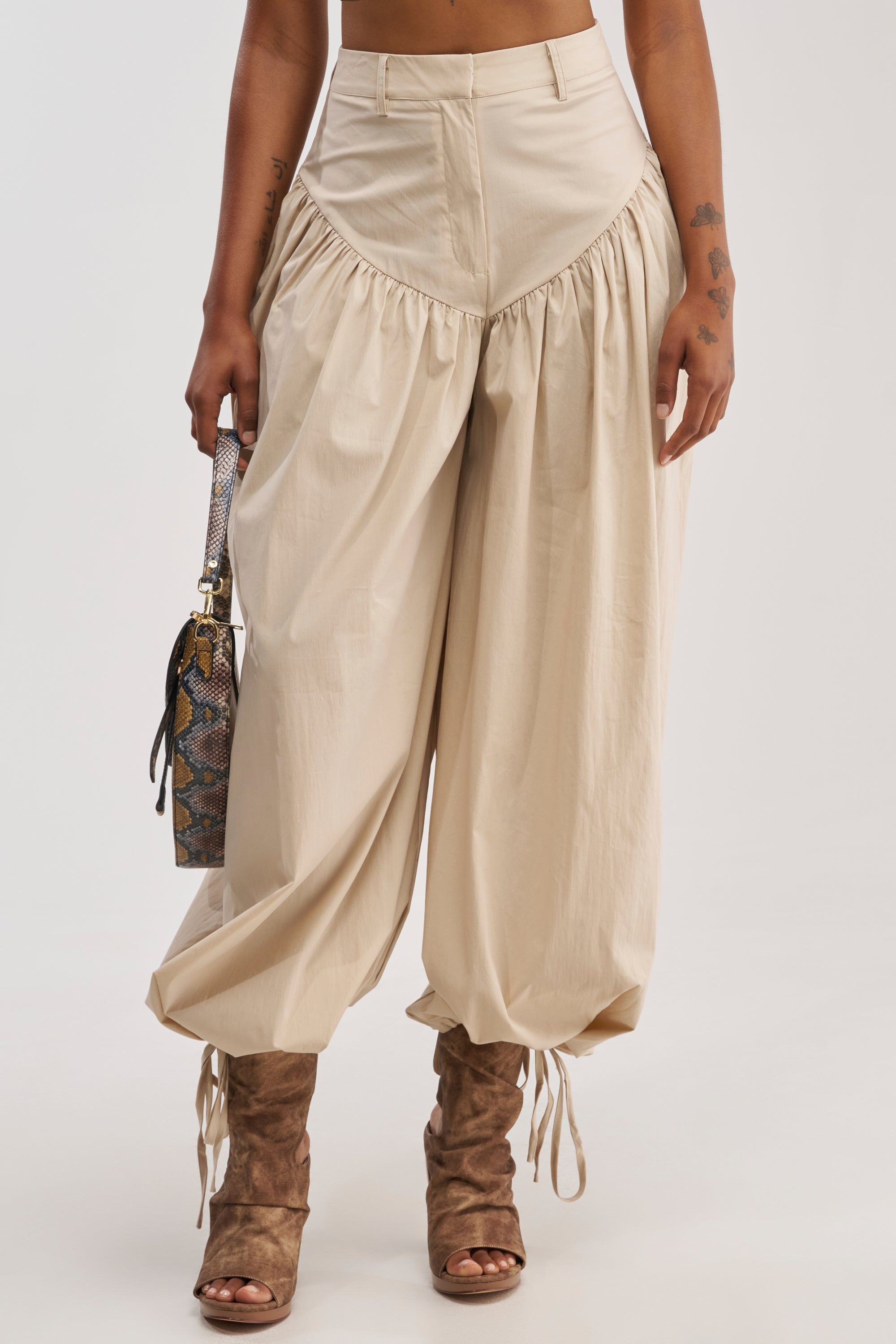 Wearing the LUCKY FOR YOU BALLOON PANT IN BEIGE, styled with brown lace-up open-toe boots and a small snakeskin-pattern handbag. Upper body is cropped out.