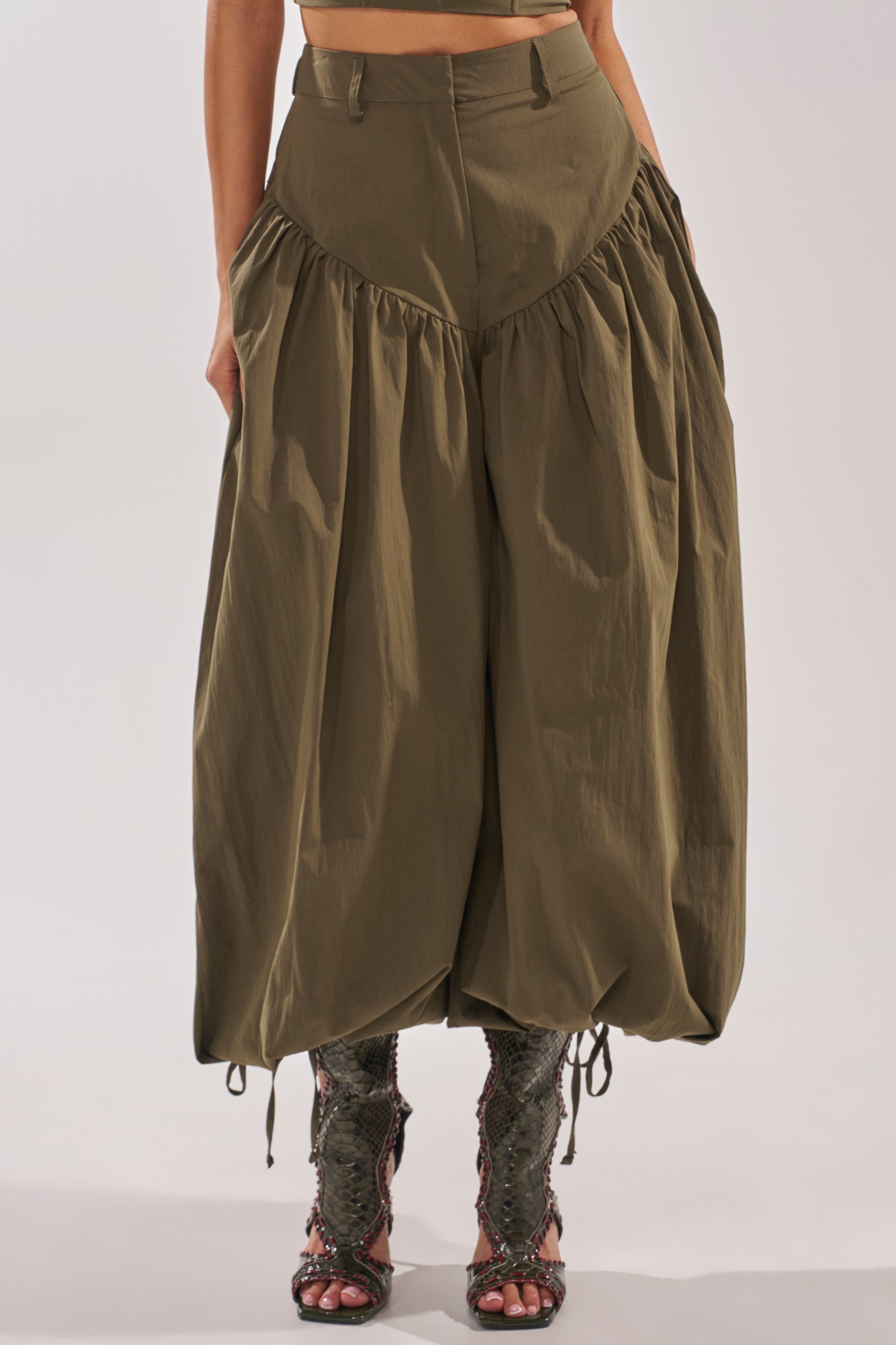 A person wears the LUCKY FOR YOU BALLOON PANT in olive green, featuring gathered seams and a high waist, paired with open-toed textured high-heeled boots. The upper body is not fully visible. 1
