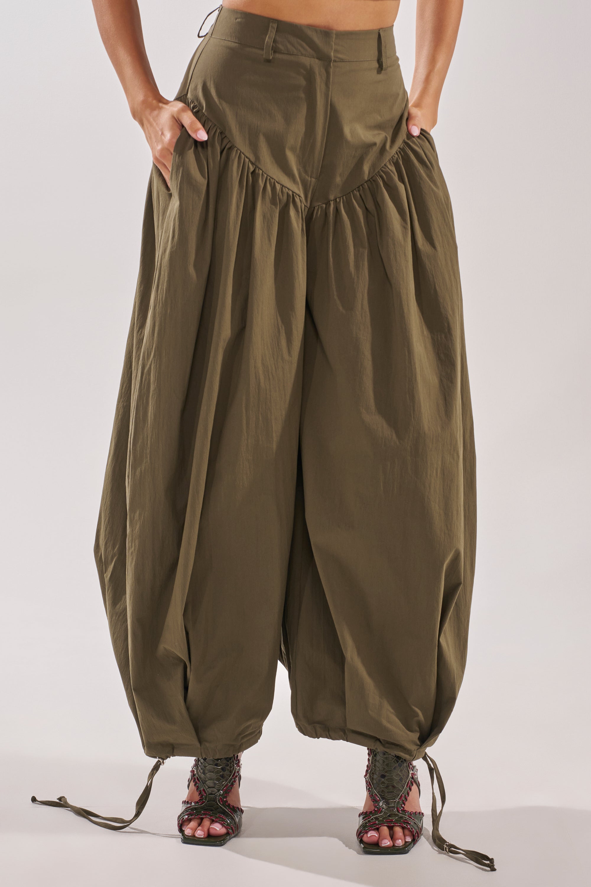 Wearing the LUCKY FOR YOU BALLOON PANT in olive green with a high waist, wide legs, gathered fabric, and drawstring hems, styled with open-toe lace-up sandals and hands in pockets for a relaxed streetwear vibe. 3