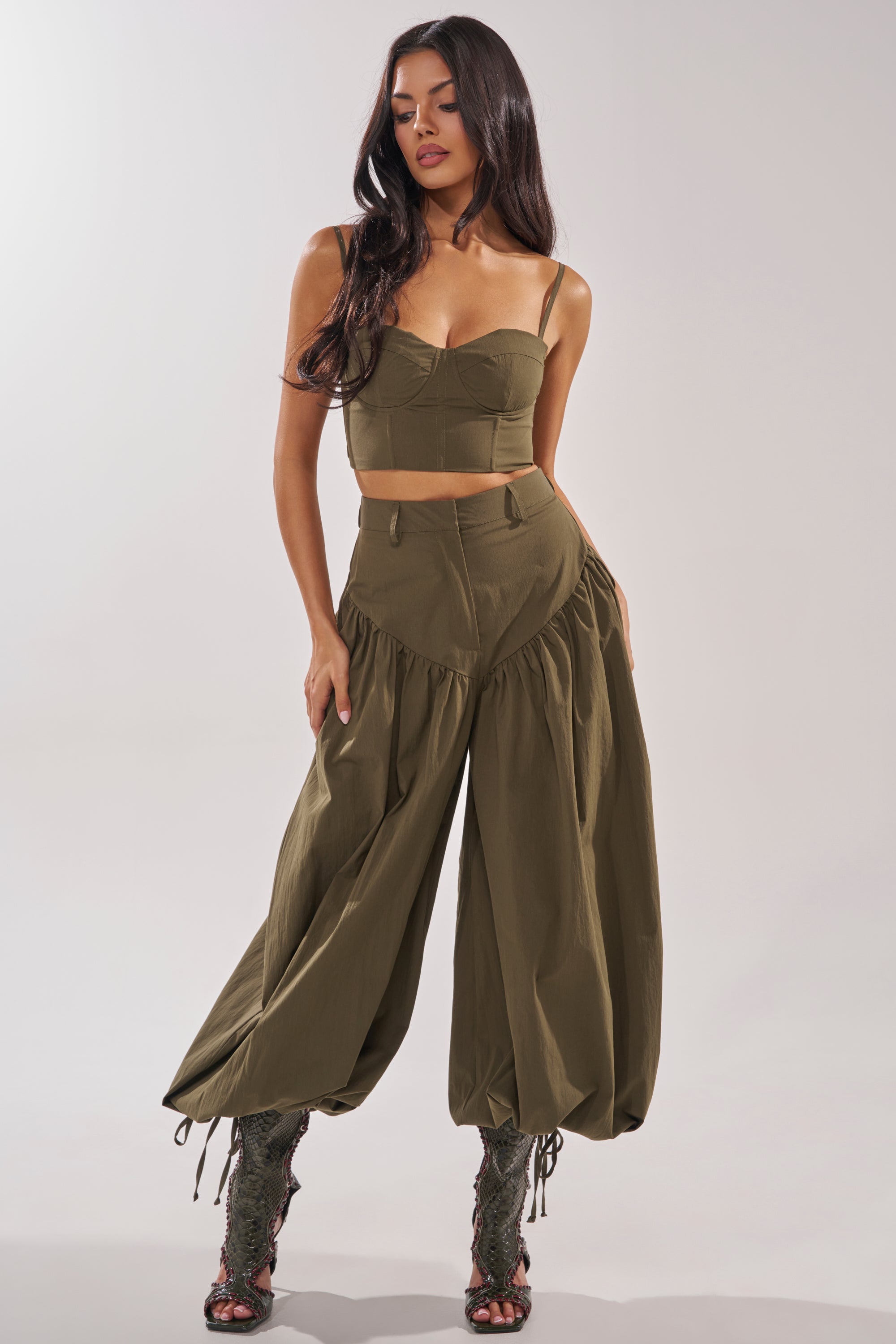 A woman poses in the LUCKY FOR YOU BALLOON PANT—olive green with gathered details—paired with a matching crop top and lace-up, open-toe boots against a plain light background. 6