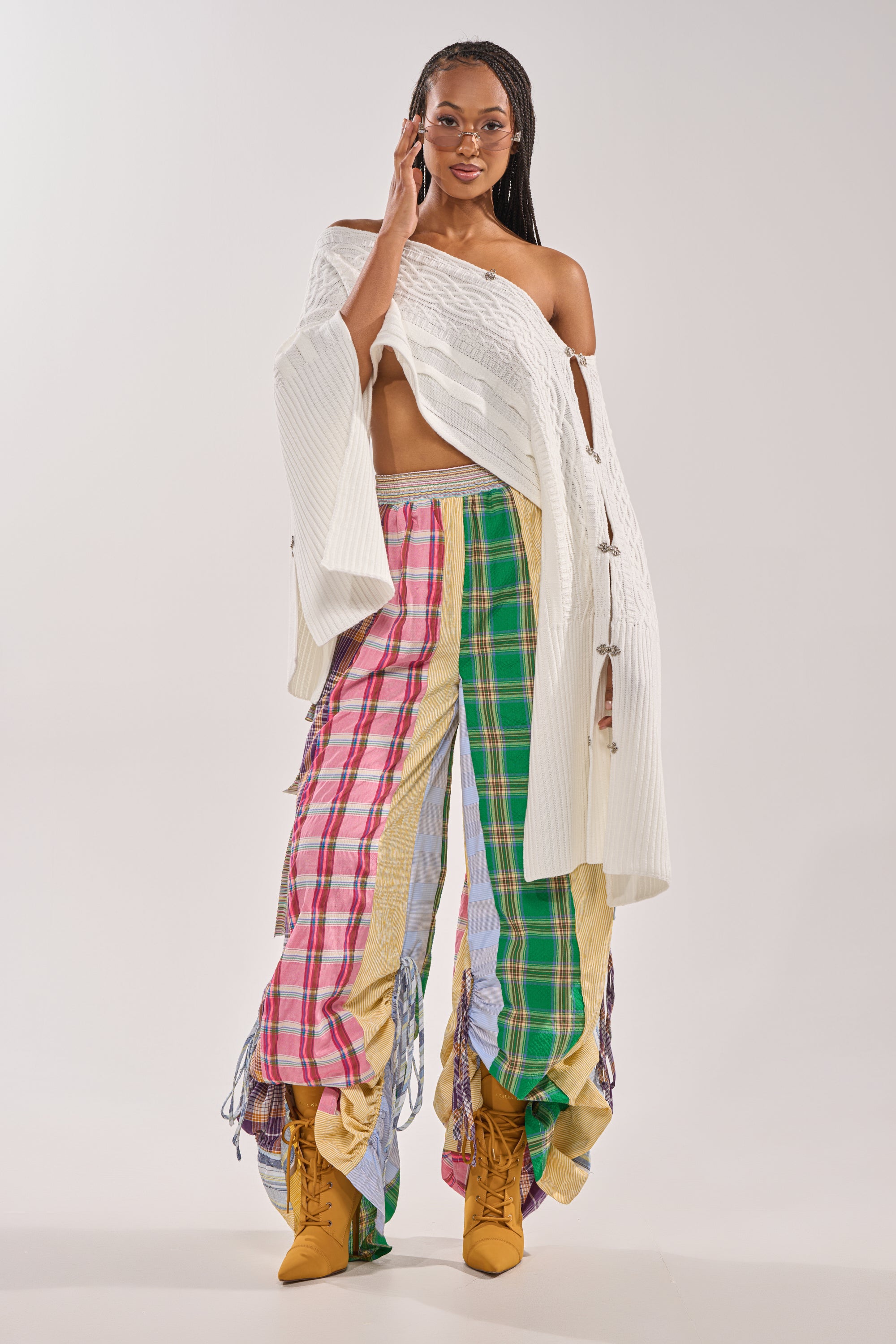 A woman in glasses and a white off-shoulder sweater confidently models the MIXED PLAIDS JOGGER with yellow lace-up boots against a plain light background. 8