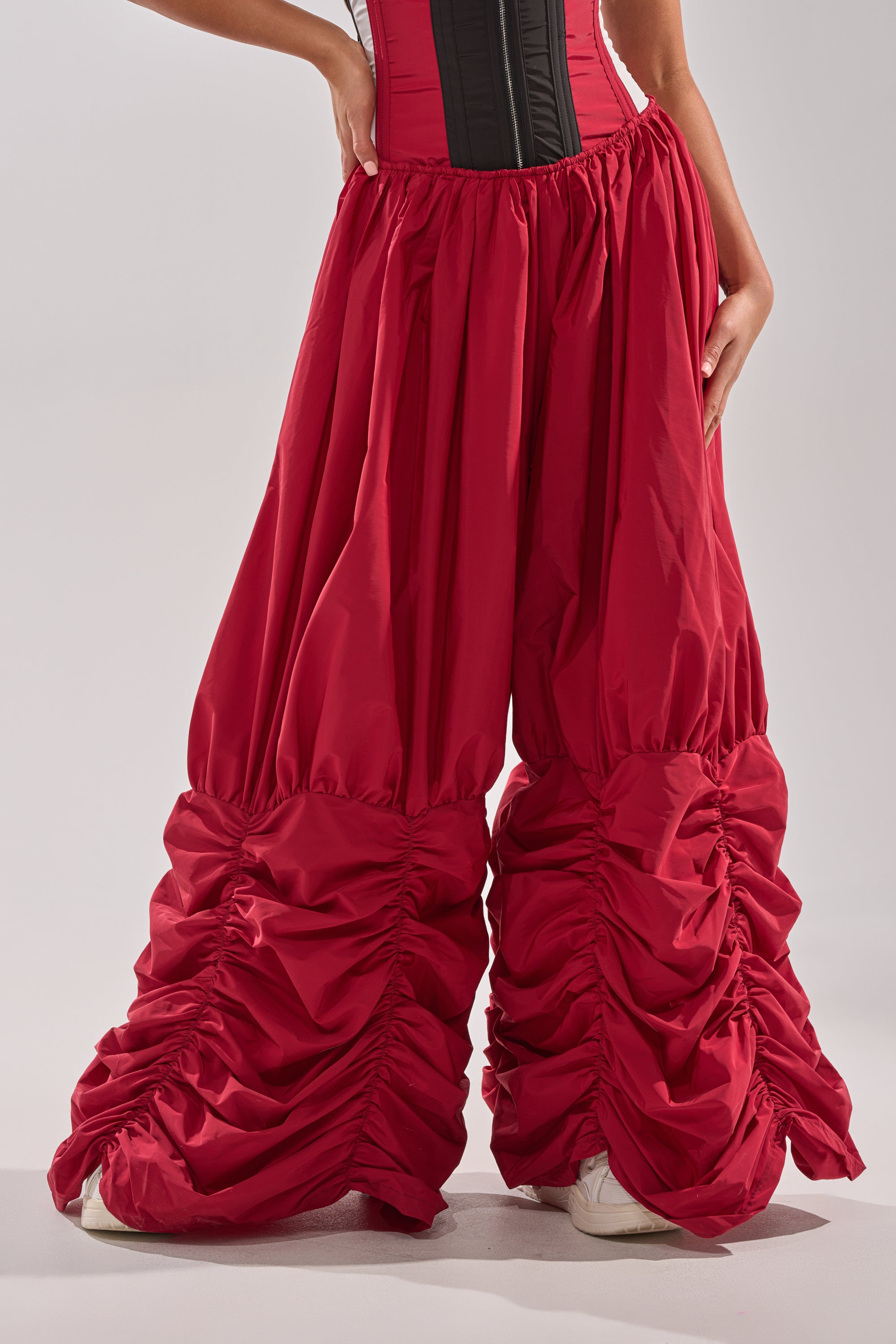 Person wearing DON'T MIND ME STACKED JOGGER in bright red with voluminous, ruched fabric gathered at the ankles; only the lower half of the body is visible, styled with a black and red corset top. 1