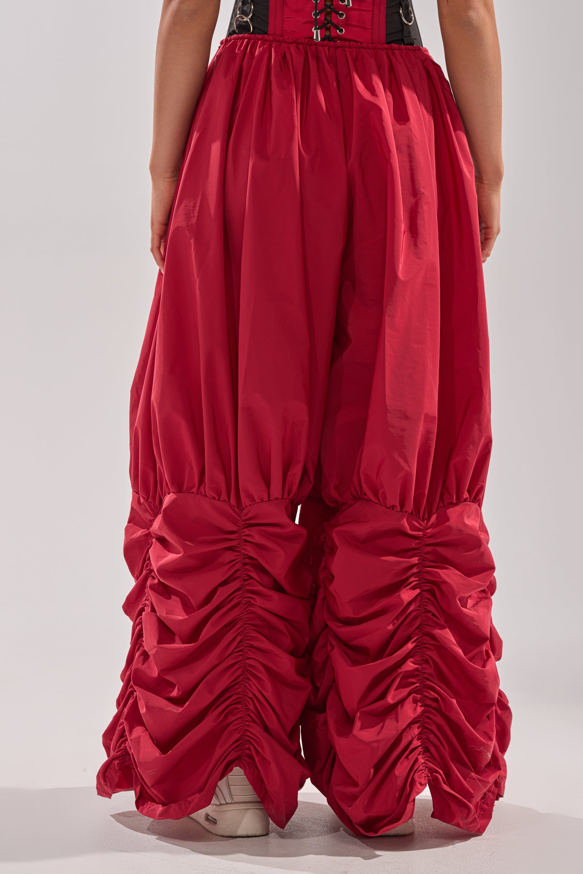 A person is shown from the back wearing DON'T MIND ME STACKED JOGGER pants in bright red, featuring ruched, gathered detailing at the knees and lower legs. White sneakers are partially visible beneath the joggers. 5