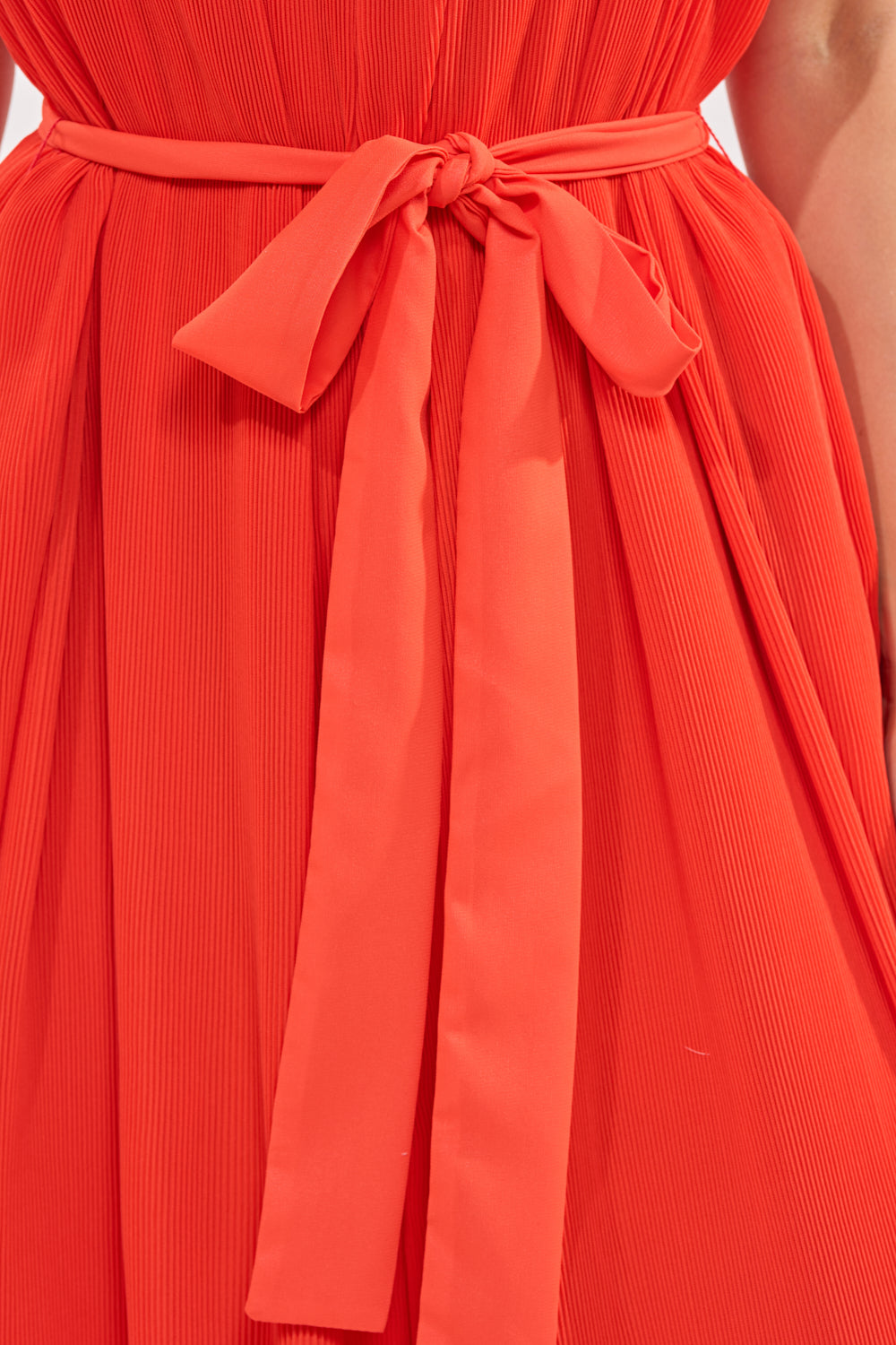Close-up of the VACATIONING PLEATED JUMPSUIT IN ORANGE, featuring bright pleats and a matching fabric belt tied in a bow at the waist. 4