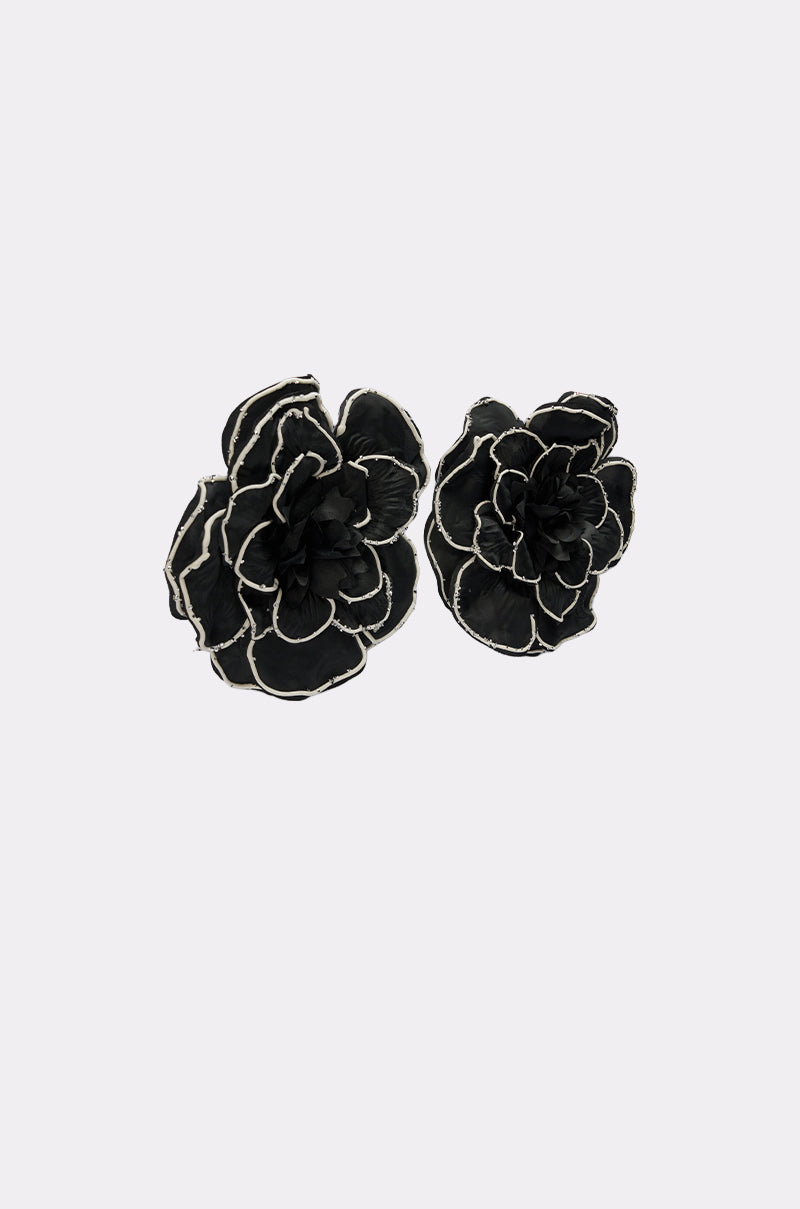 A pair of DRAMA EARRING black fabric flower hair clips with white trim edges, displayed on a plain light gray background.
