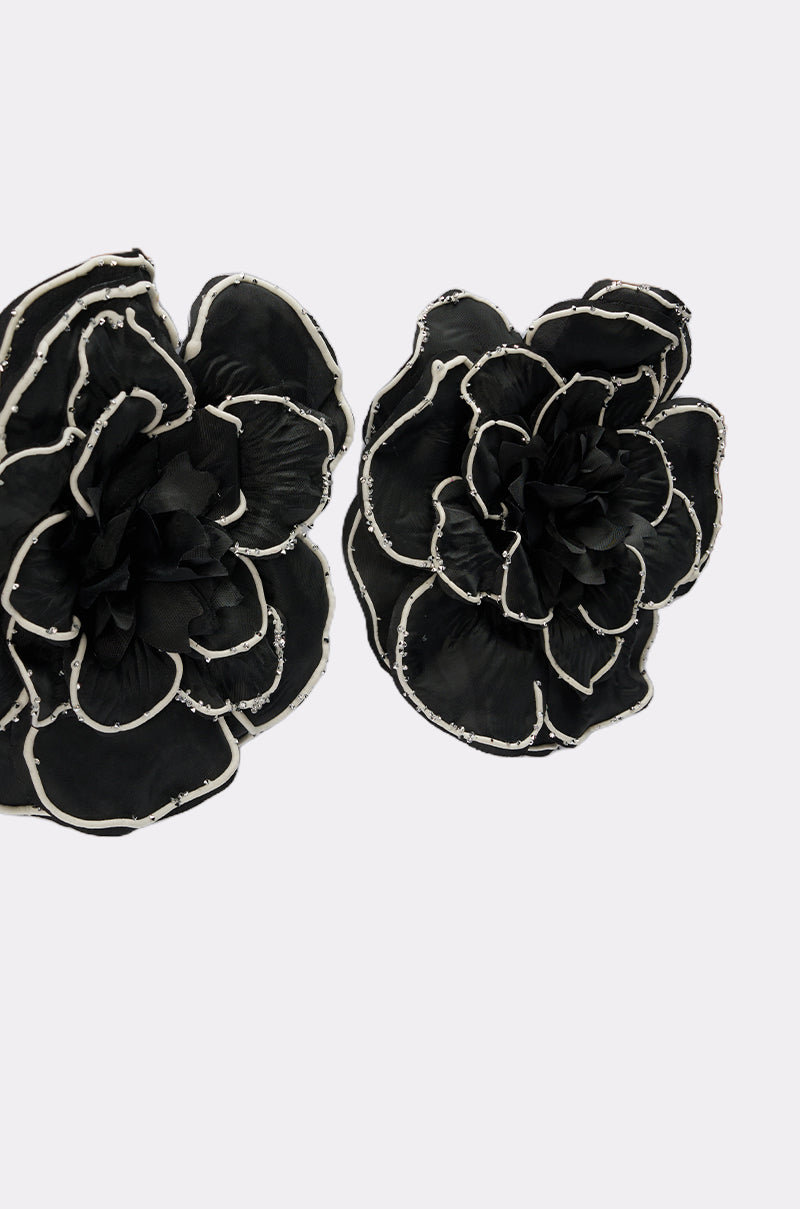 Two DRAMA EARRING pieces featuring large black fabric flowers with white-edged, layered petals overlap each other against a plain light background.