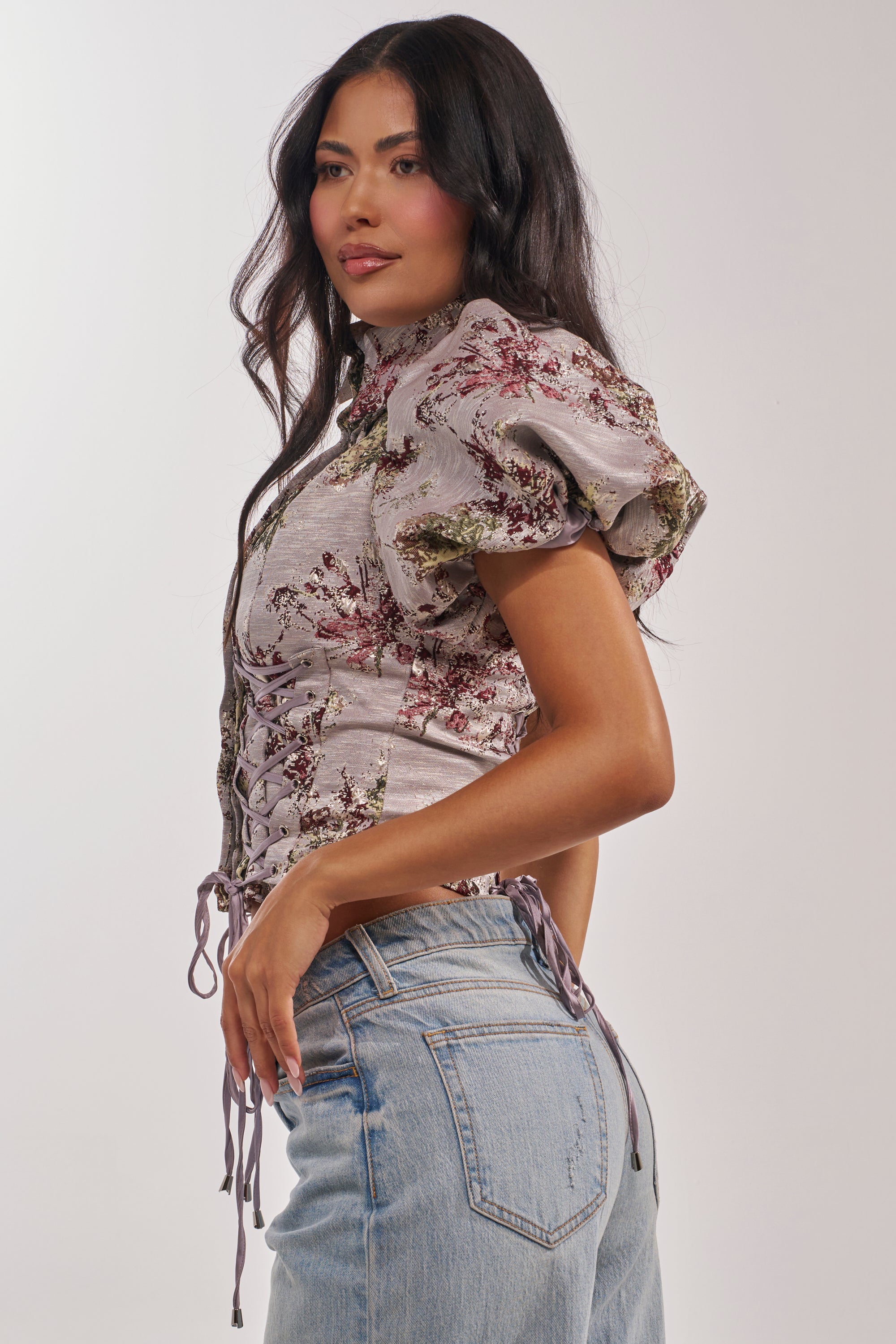 A woman with long wavy hair wears the DARLING FLORAL BROCADE PUFF SLEEVE BLOUSE and blue jeans, posing in profile against a plain background. 2