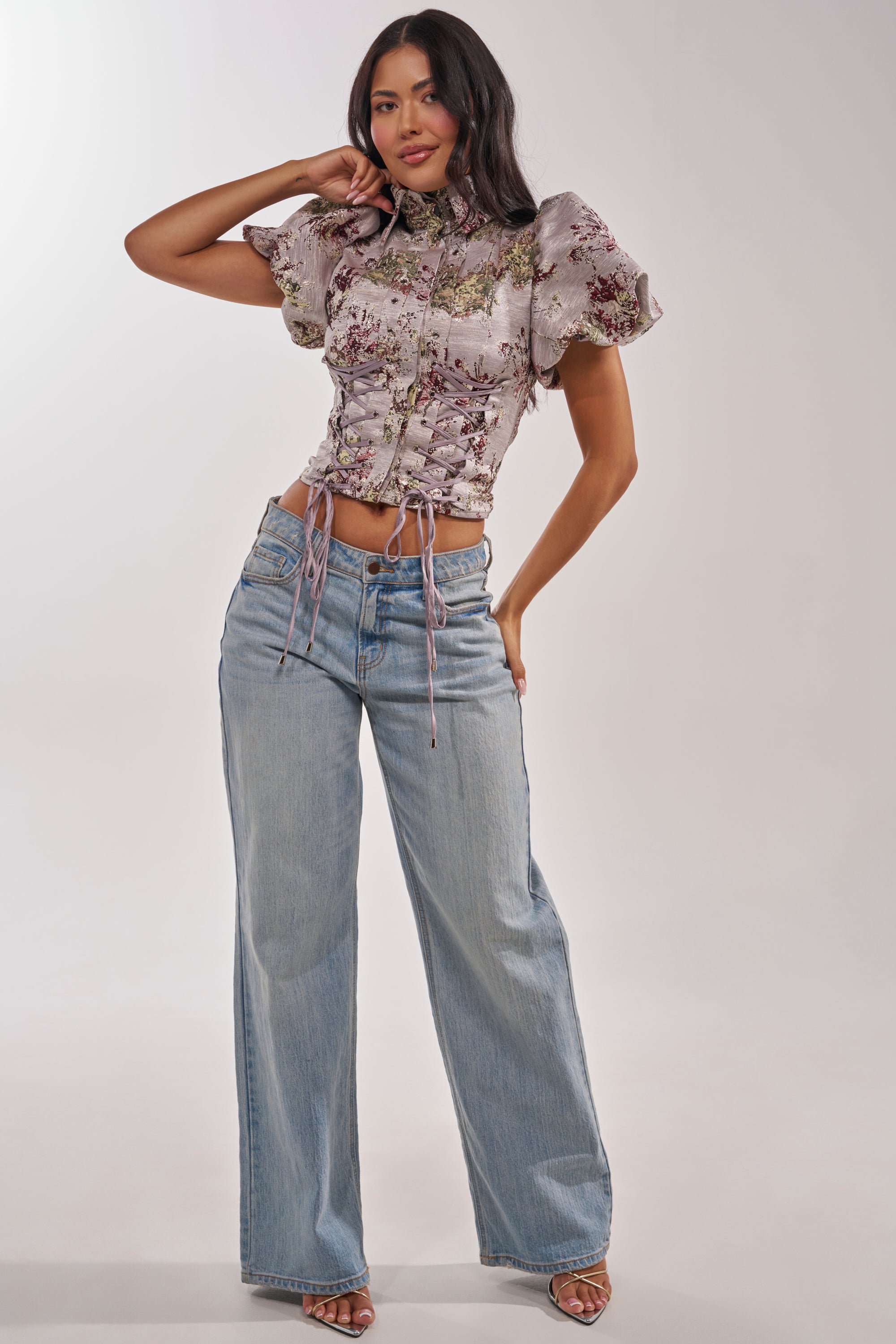 A woman poses against a plain light background wearing the DARLING FLORAL BROCADE PUFF SLEEVE BLOUSE with a fitted silhouette, paired with light blue wide-leg jeans and open-toed heels. 5