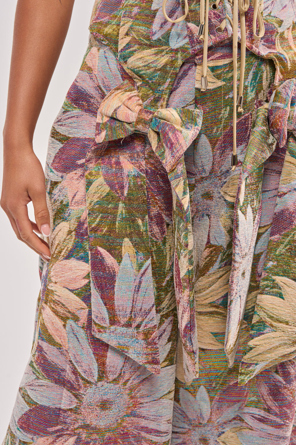 Close-up of a person wearing the SUNFLOWER FIELDS CORSET featuring a large metallic floral print in green, purple, yellow, and white with a fabric belt tied in a bow at the waist—ideal for party-ready styling. 8
