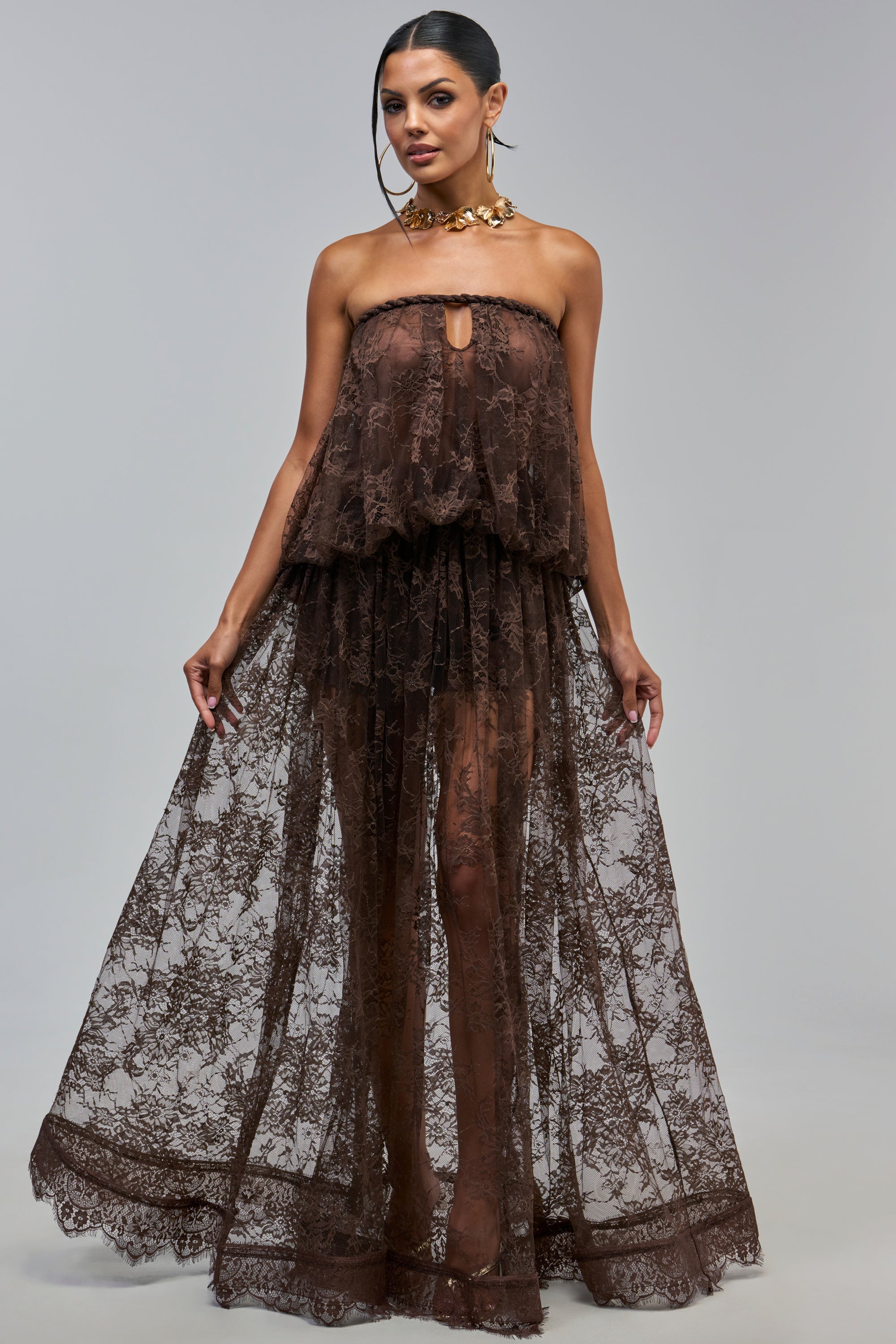 A model wears the HANNAH LACE MAXI SKIRT IN BROWN, a strapless, floor-length brown lace maxi dress with a keyhole cutout at the neckline, featuring a sheer brown floral lace design.
