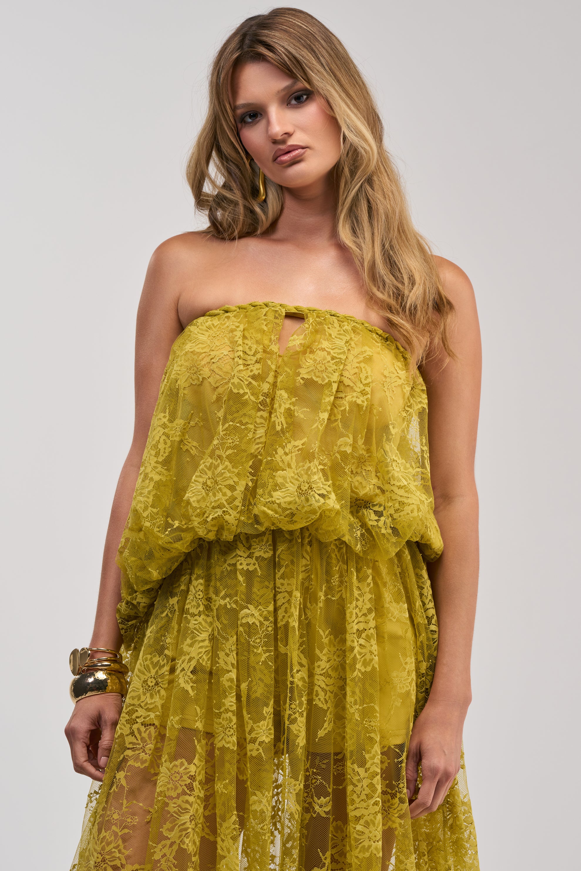 Wearing the HANNAH LACE BLOUSE, a woman with long, wavy hair and gold bracelets stands against a plain light background.