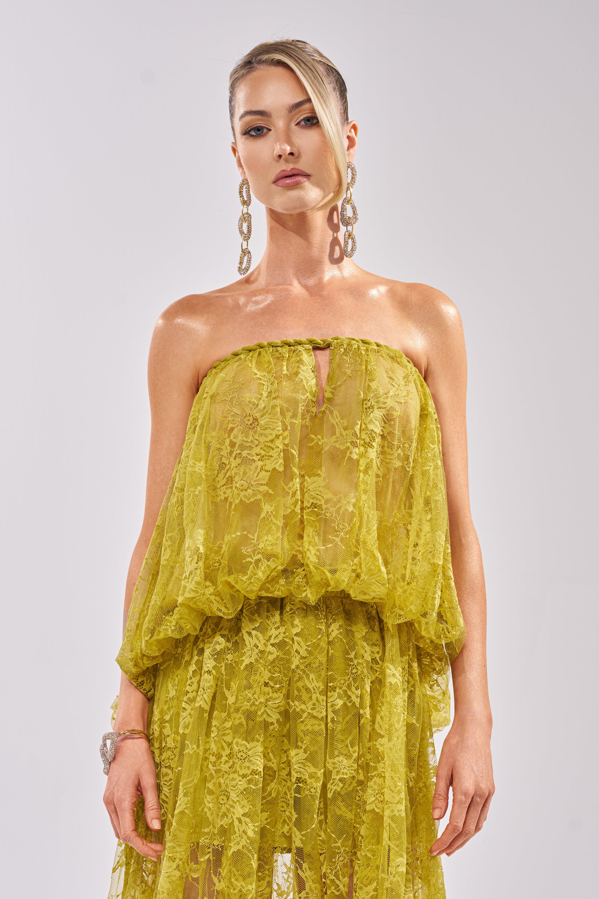 A woman confidently poses against a plain light background, wearing the HANNAH LACE BLOUSE in sheer yellow and large dangling earrings, looking directly at the camera. 3