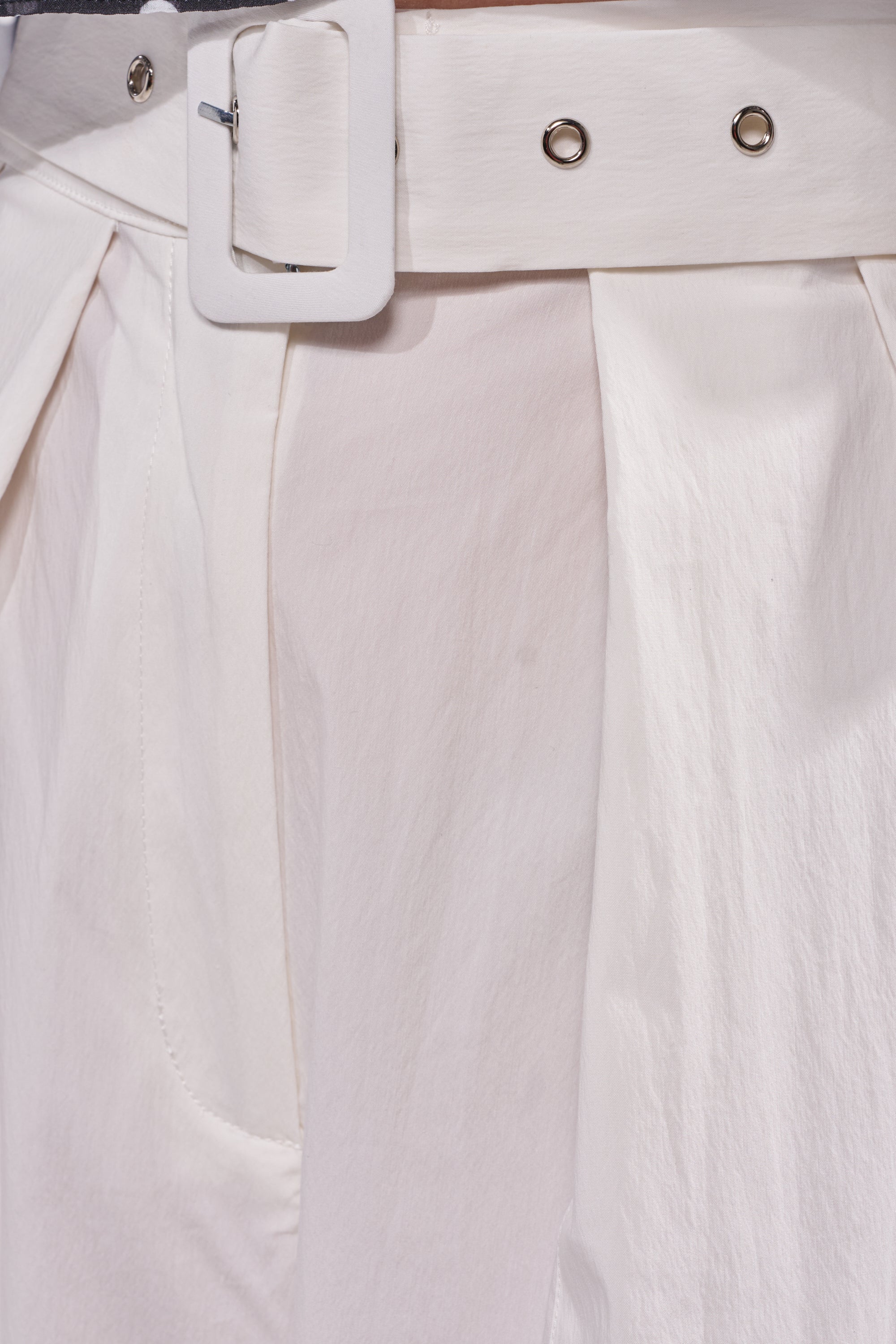 Close-up of the GIVE ME YOUR LOVE TROUSER, a high-rise white barrel pant with pleated waist, wide belt with metal eyelets and rectangular buckle, crafted in softly lustrous textured fabric. 7