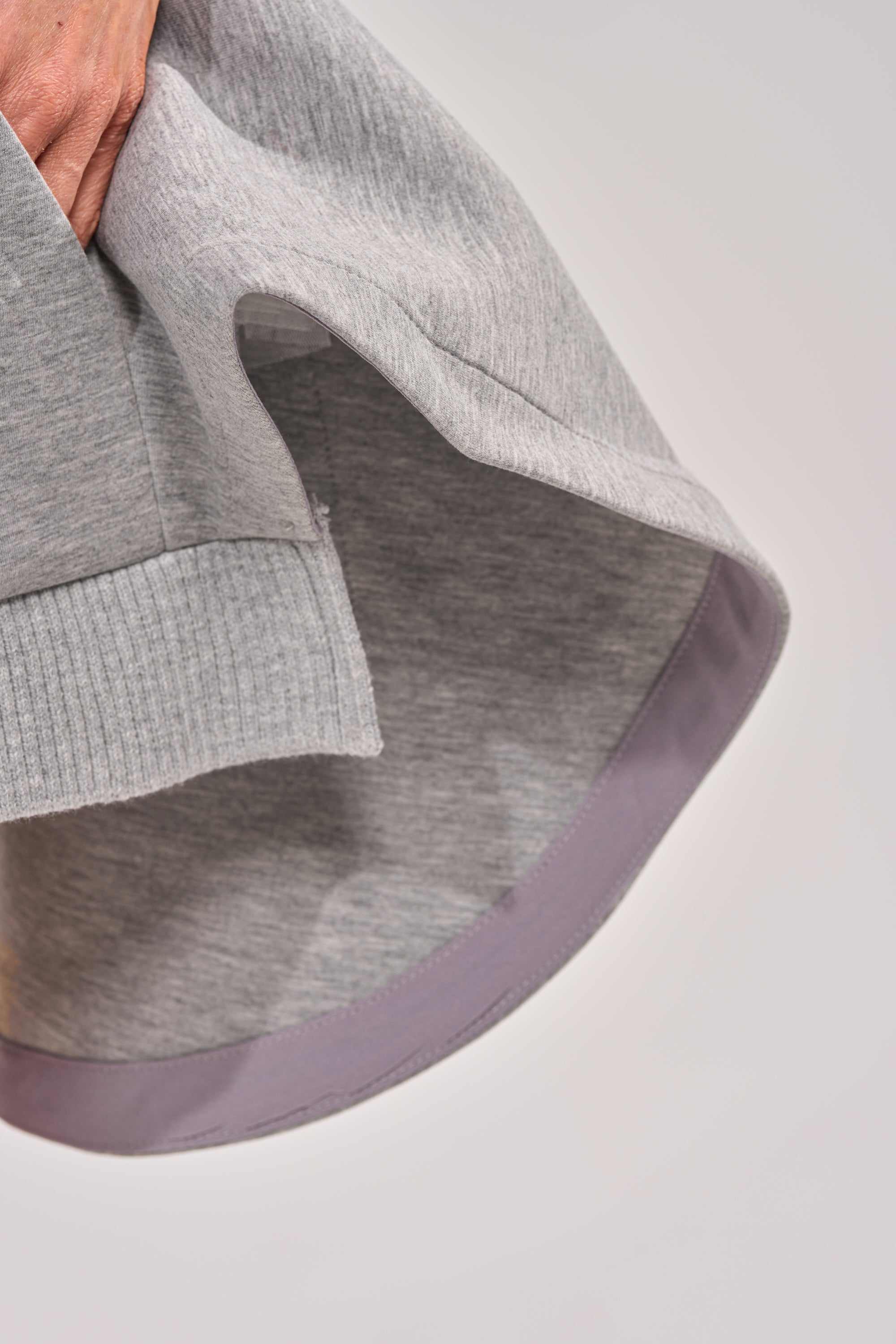A close-up of a hand holding the edge of the NO WORK ALL PLAY SCUBA SKIRT, highlighting its grey knit fabric, ribbed hem, and a touch of lavender lining—perfect for casual everyday style. 5