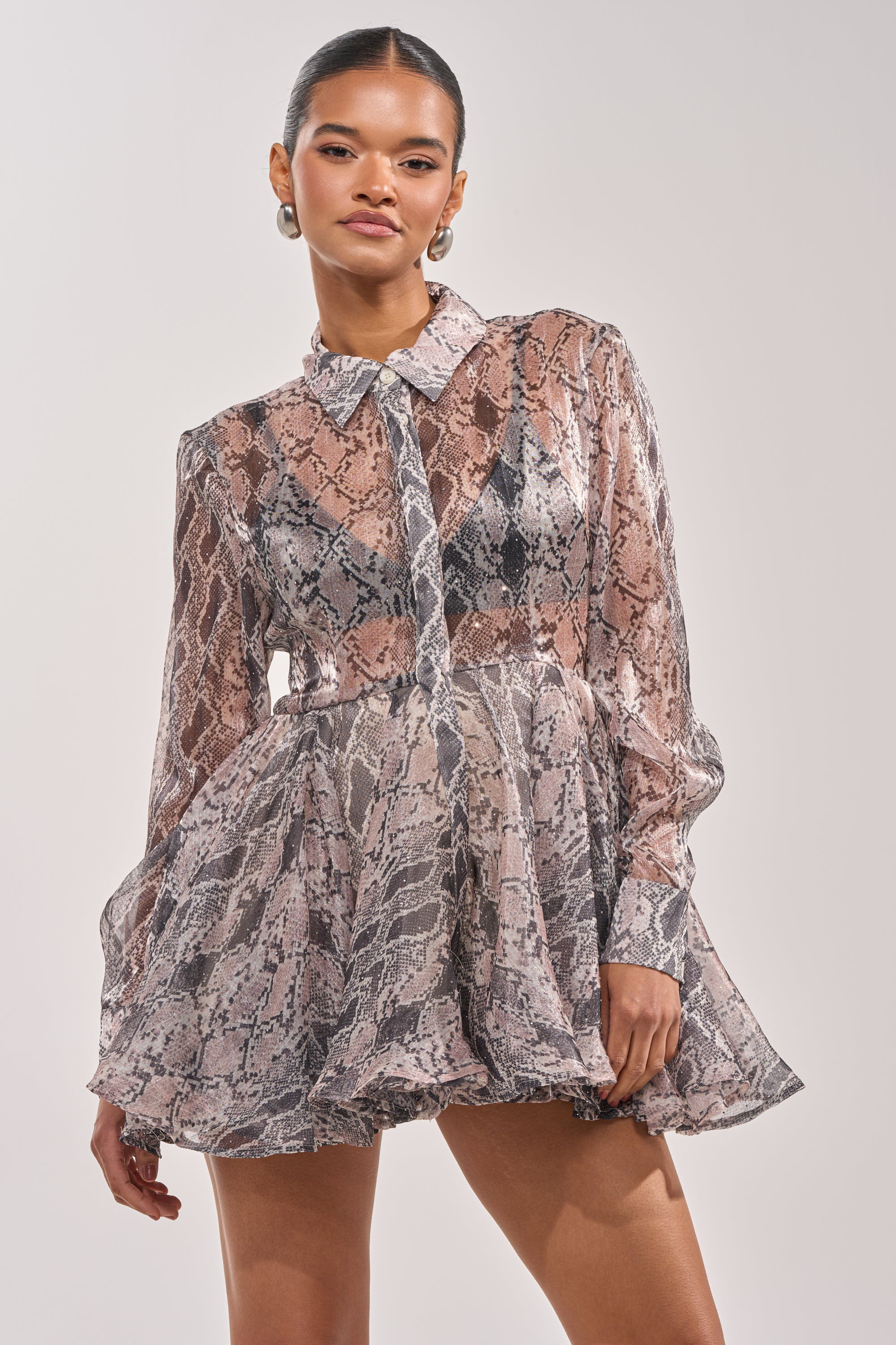 A woman stands confidently against a light background wearing the WILD RHYTHM SNAKE PRINT MINI DRESS, featuring sheer long sleeves, a collared neckline, and a striking fit-and-flare silhouette. 2