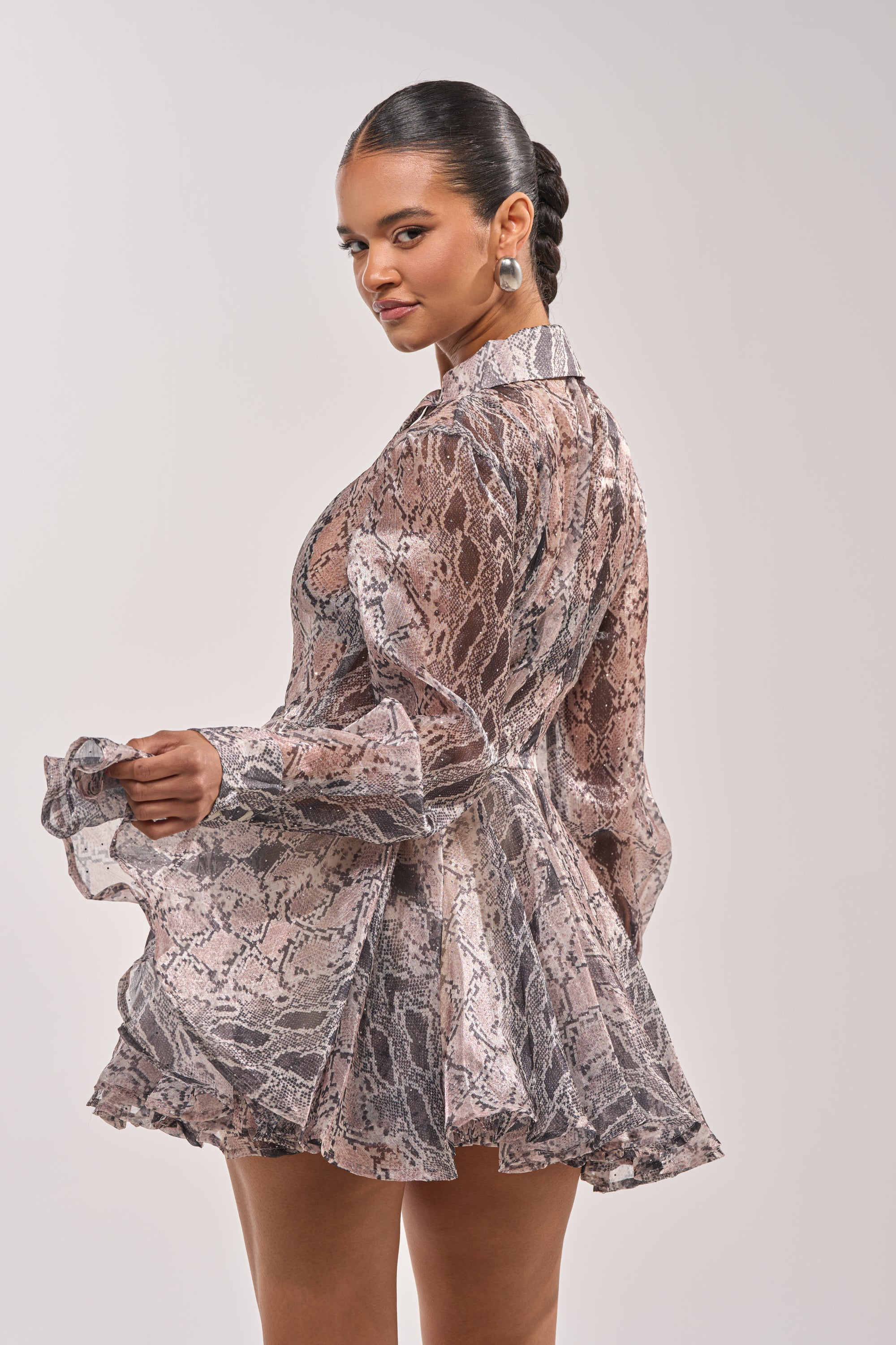 A woman with slicked-back hair and silver earrings models the WILD RHYTHM SNAKE PRINT MINI DRESS, featuring rhinestone embellishments, as she poses against a plain light background. 4
