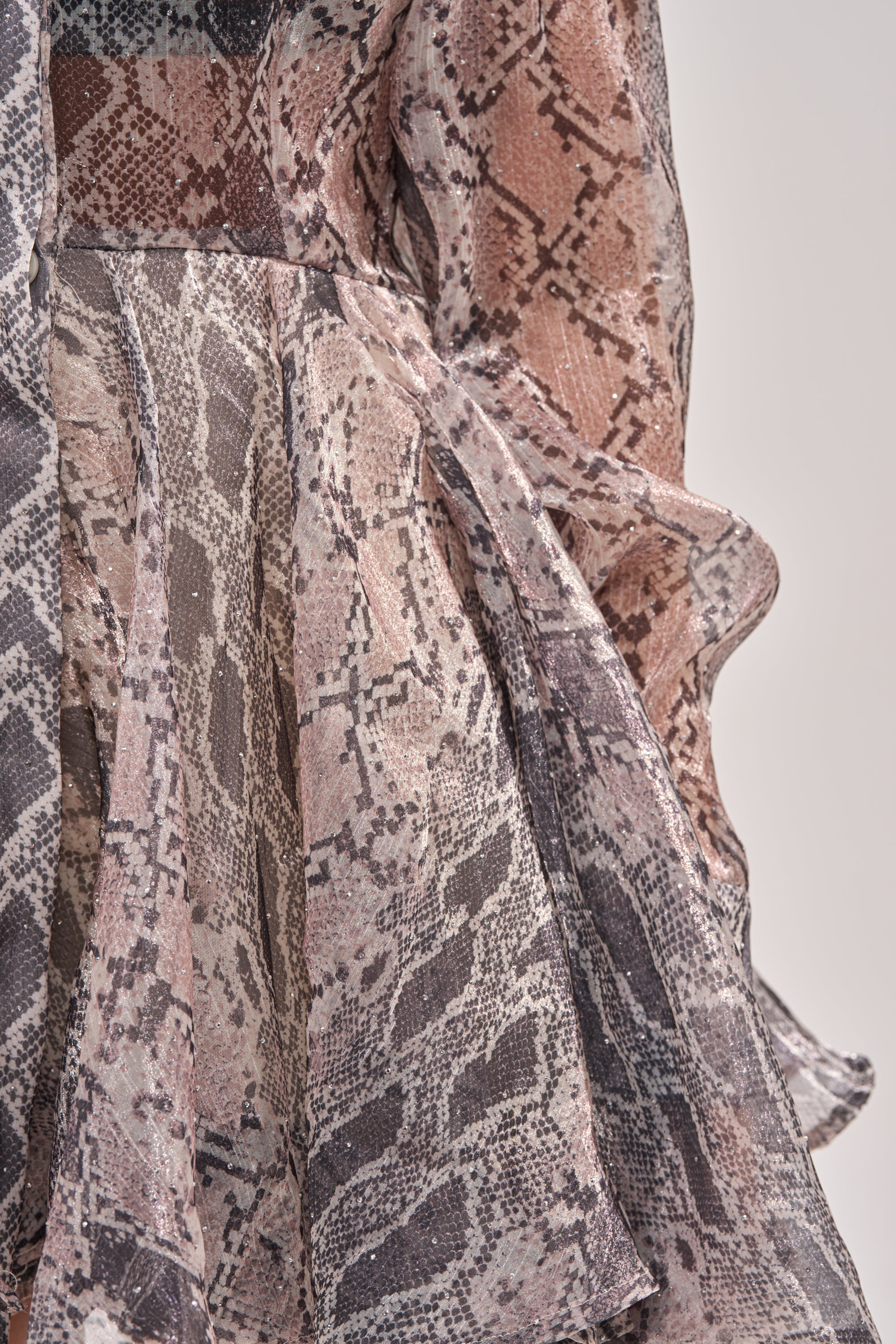 Close-up of the WILD RHYTHM SNAKE PRINT MINI DRESS, featuring flowing, ruffled fabric with a brown, beige, and grey snakeskin pattern. The light, semi-sheer material drapes in soft folds for effortless movement and chic style. 8