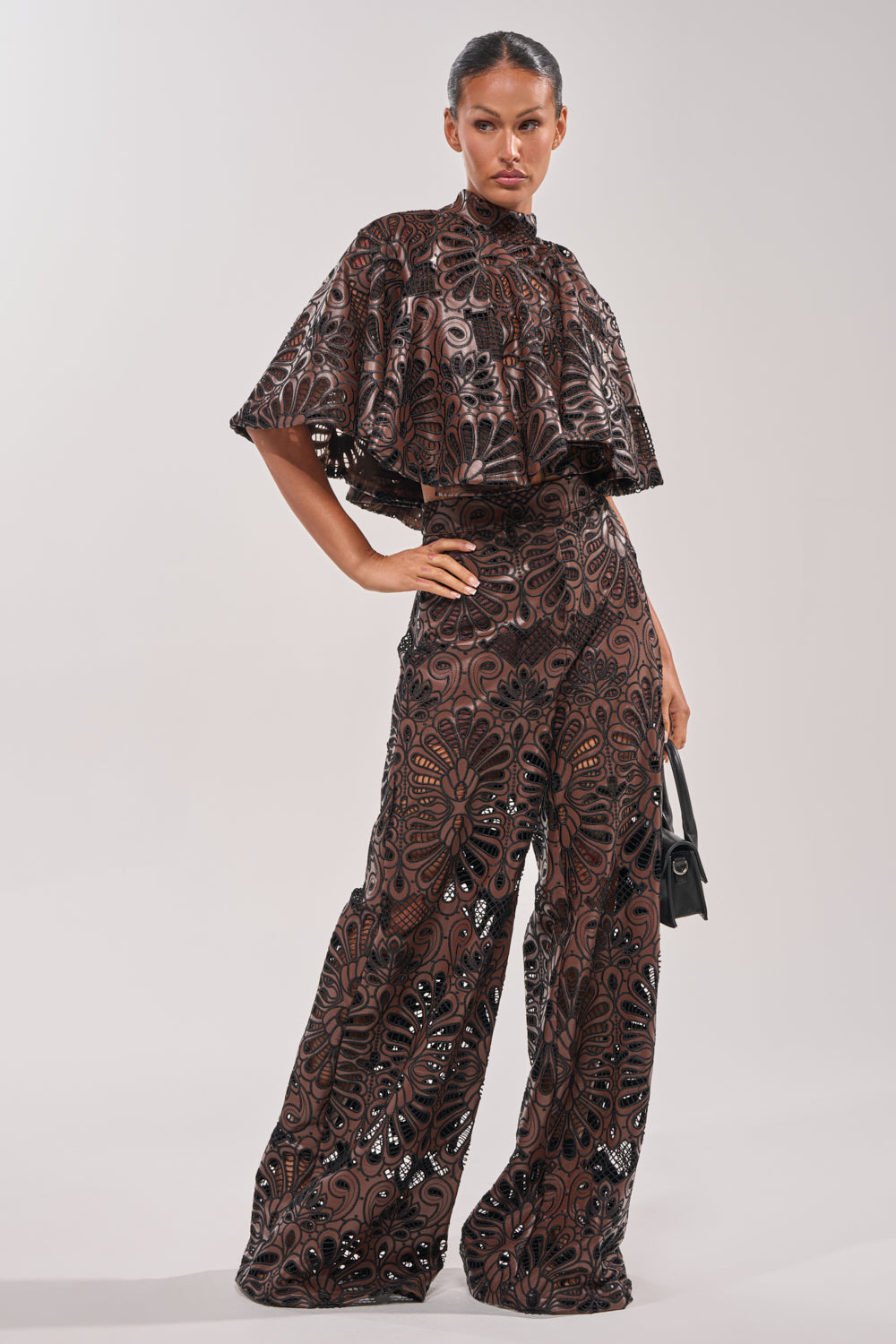 A woman poses confidently in the LENA LACE AND PU BLOUSE with matching wide-leg pants, featuring intricate lace details—styled with a small black handbag, perfect for evening events. 5