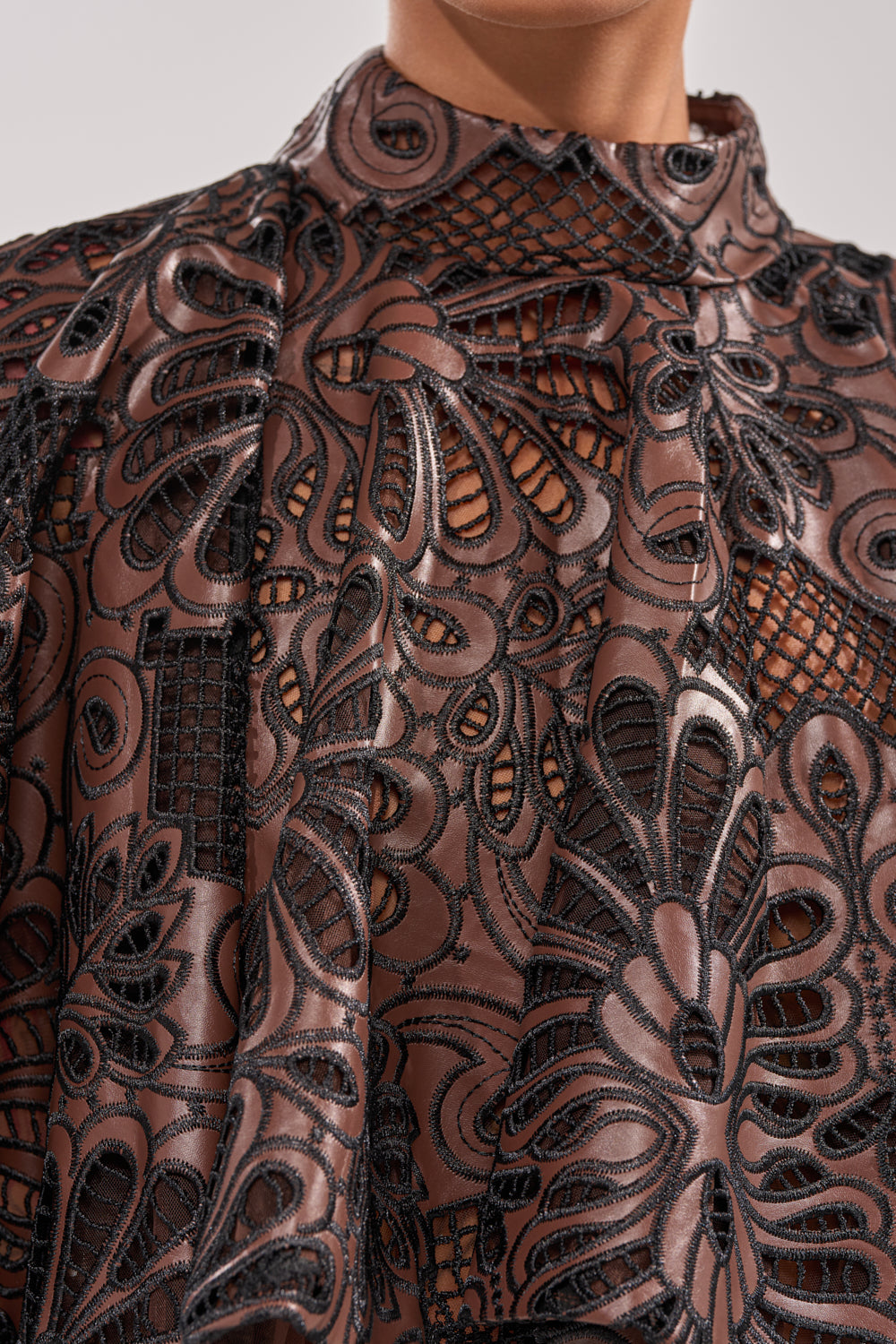 A close-up of a person wearing the LENA LACE AND PU BLOUSE—a sheer, high-collared top featuring intricate black lace over brown fabric that subtly reveals skin. 8